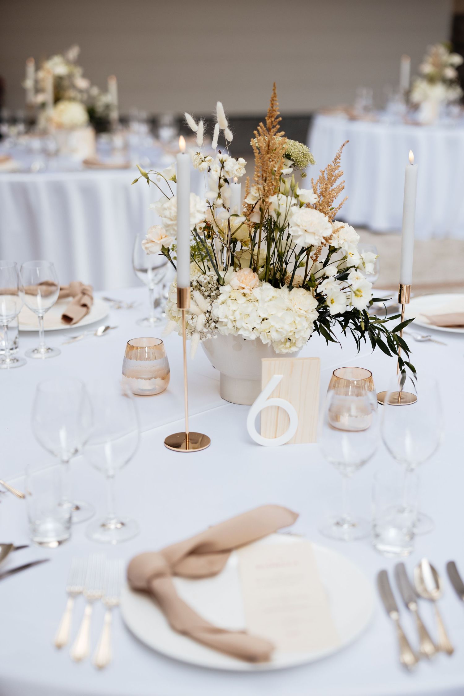 Elegant wedding table setting with white floral centerpiece, candles, and neutral decor.