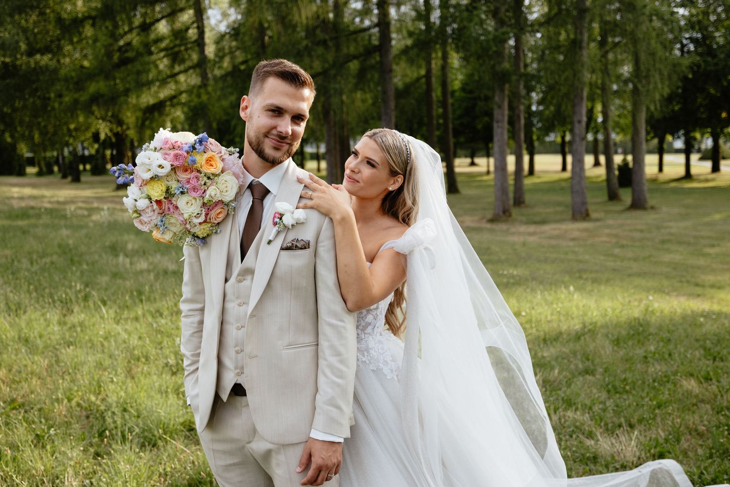 Wedding couple embracing in a lush green park setting with colorful floral bouquet.