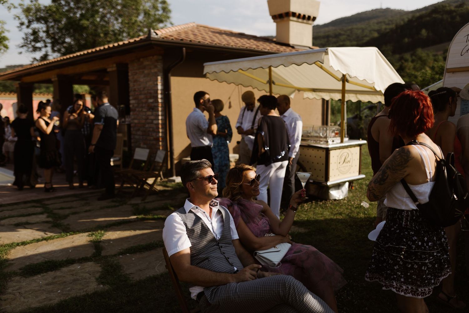 Outdoor wedding reception gathering with guests mingling in natural sunlight.