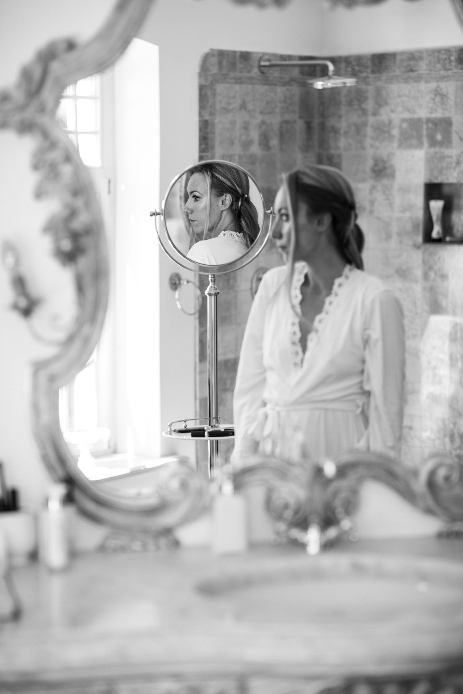 Black and white reflection in vintage mirror showing bridal preparation scene in elegant room.