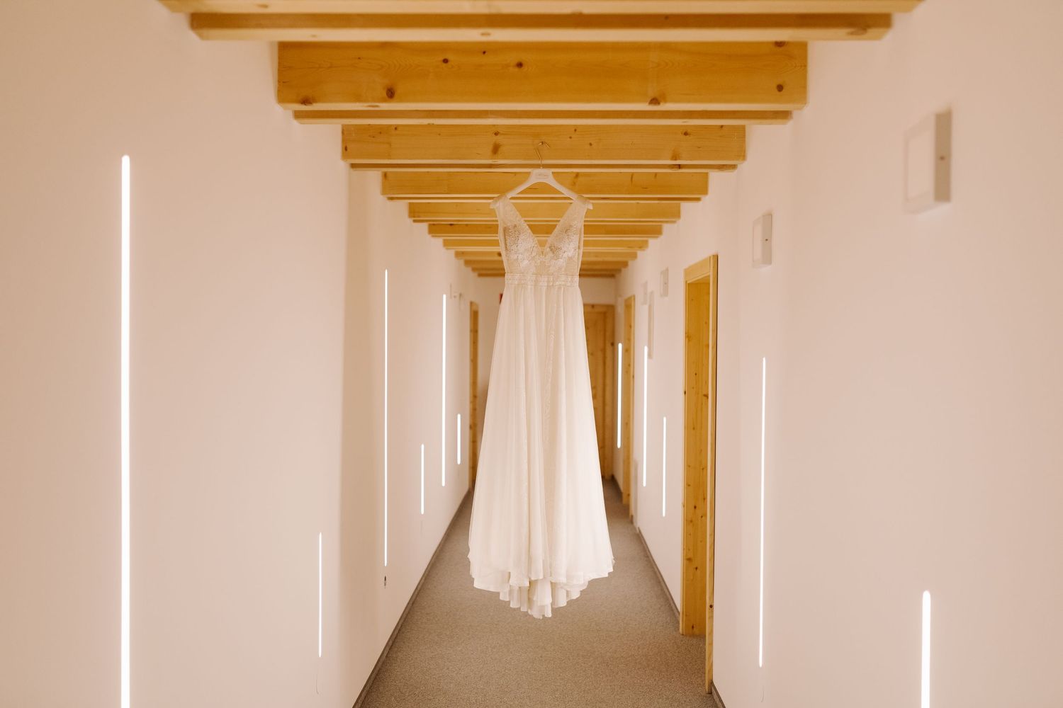 A long white hallway with wooden beams on the ceiling and a bright window at the end creates a dramatic perspective.