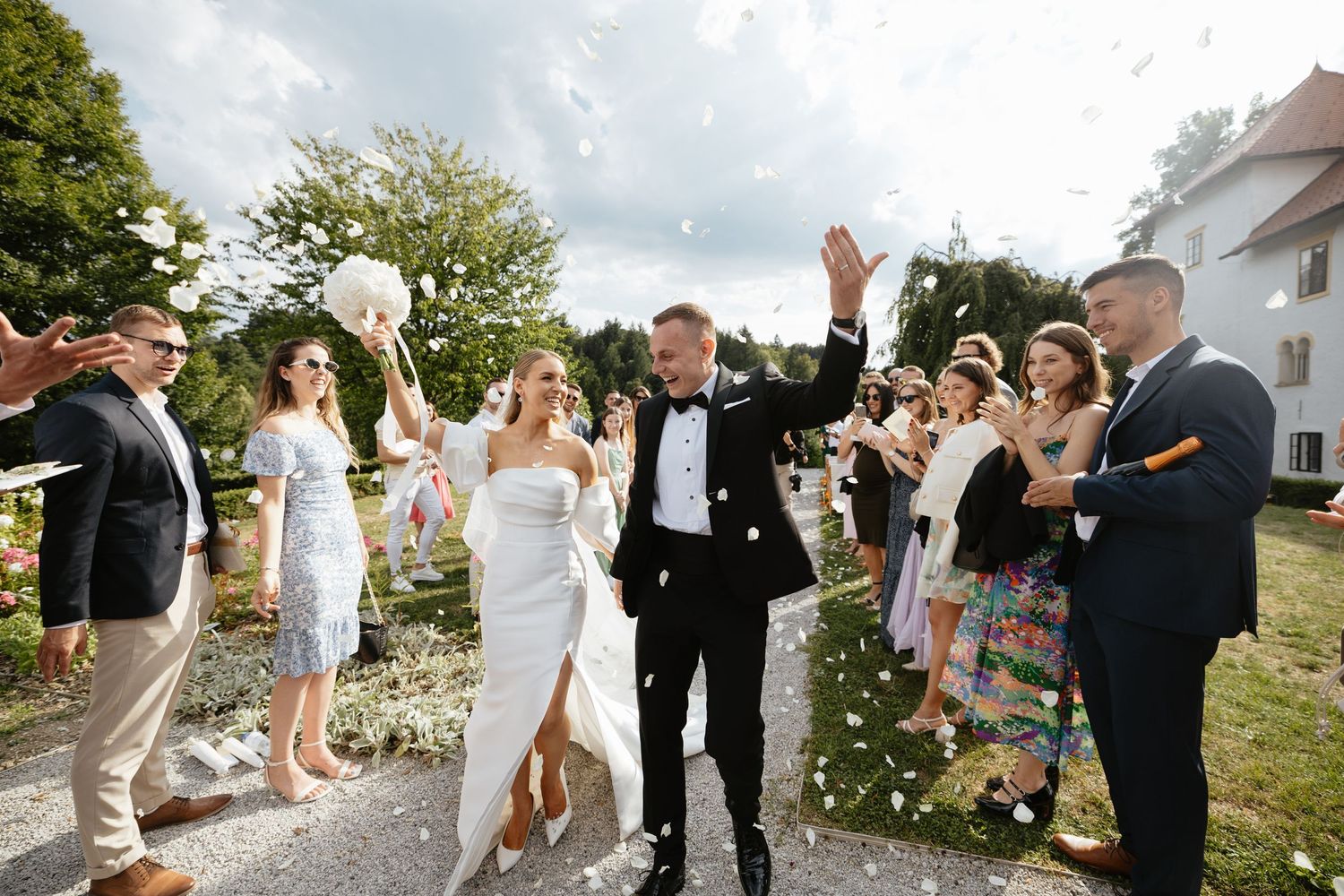 Joyful newlyweds walk through confetti shower as wedding guests celebrate outdoors at elegant venue.