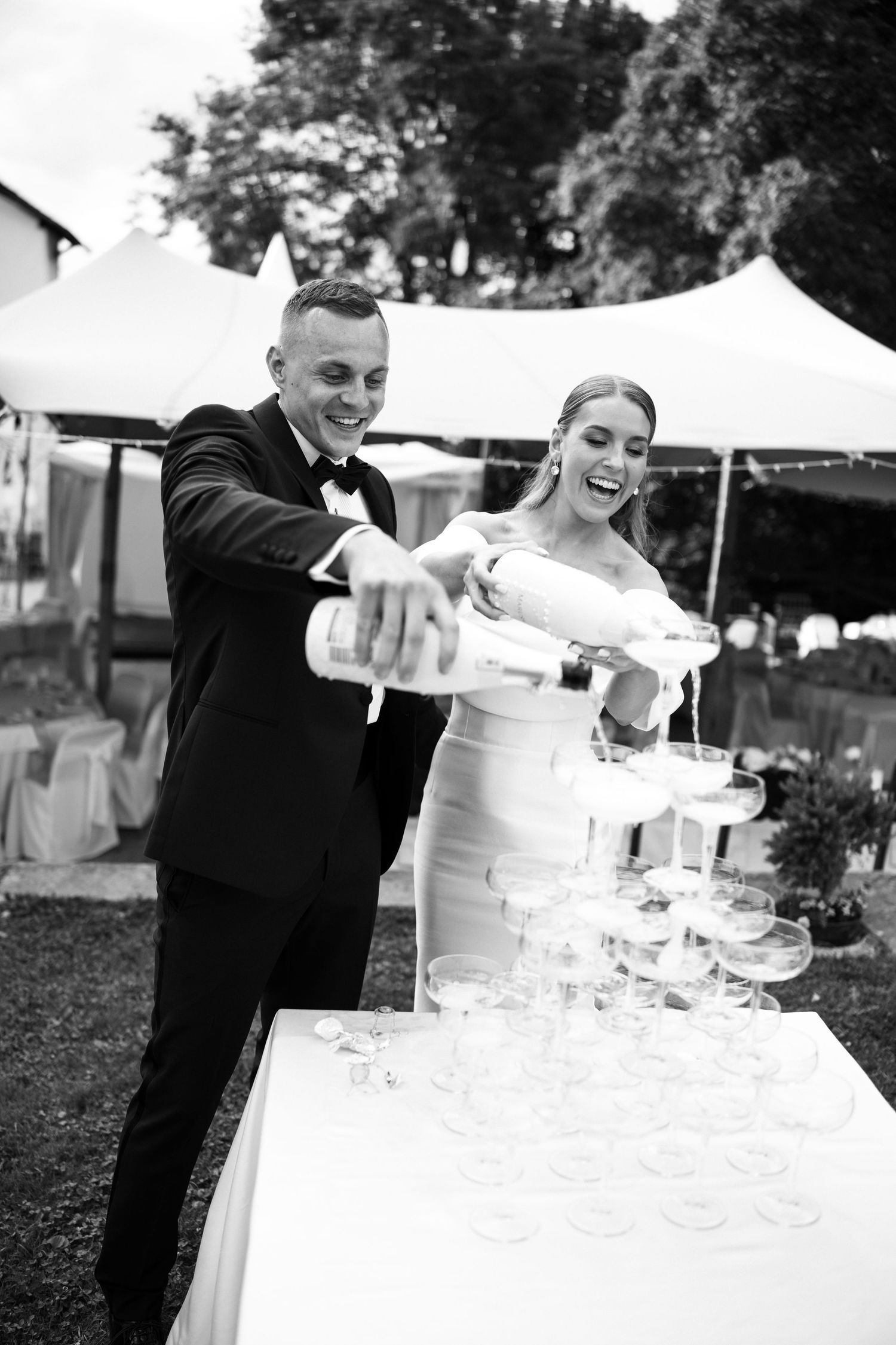 Wedding couple pouring champagne into a tower of glasses at their reception.