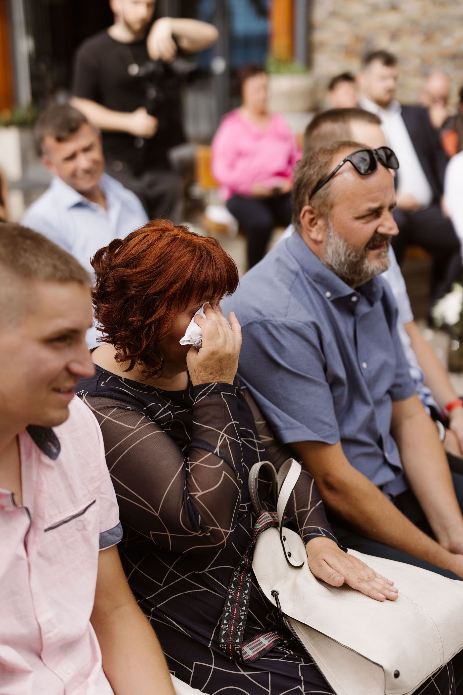 Wedding guests laugh and react emotionally during an outdoor ceremony.
