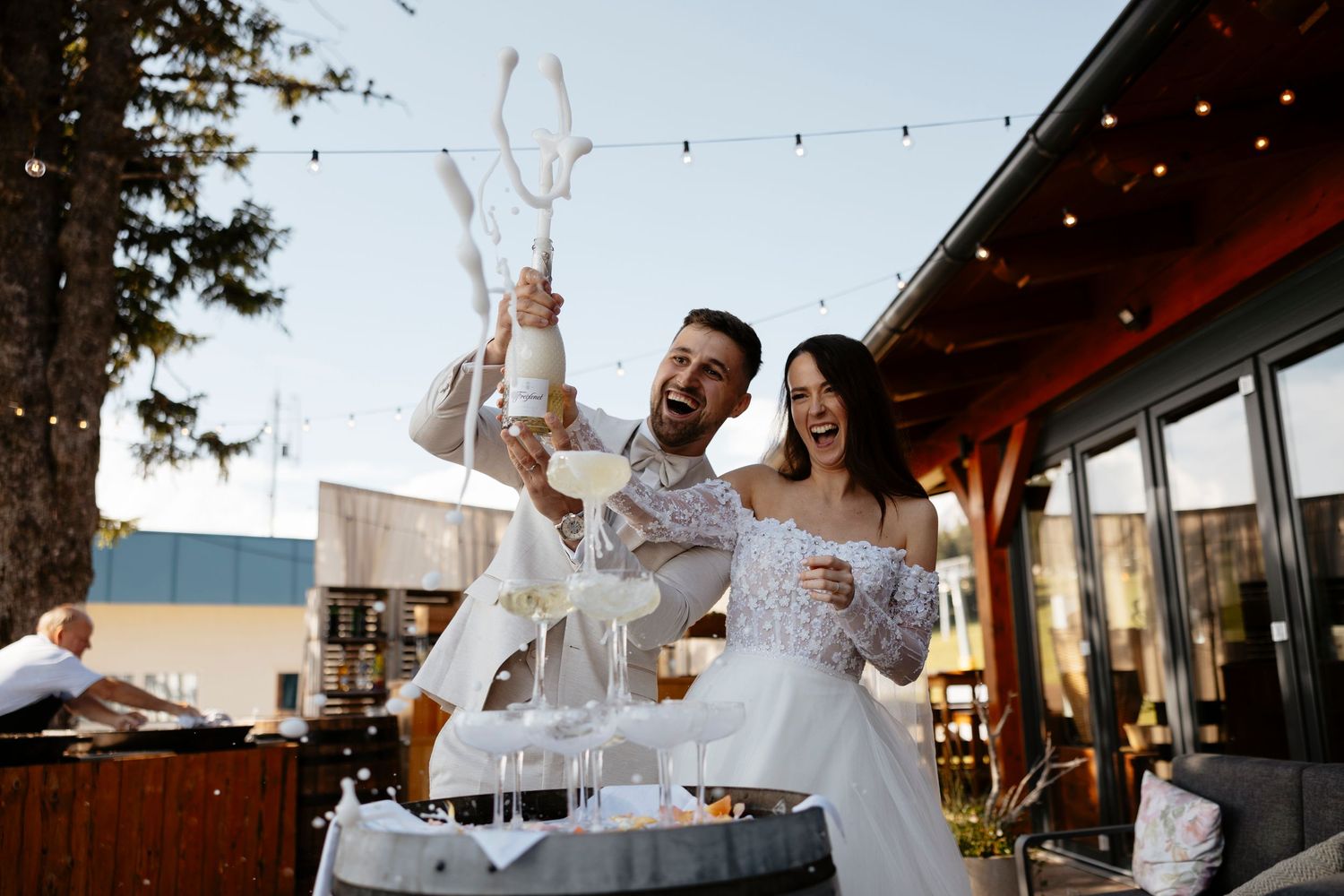 Wedding party celebrates joyfully with raised arms on an outdoor patio during sunset reception.