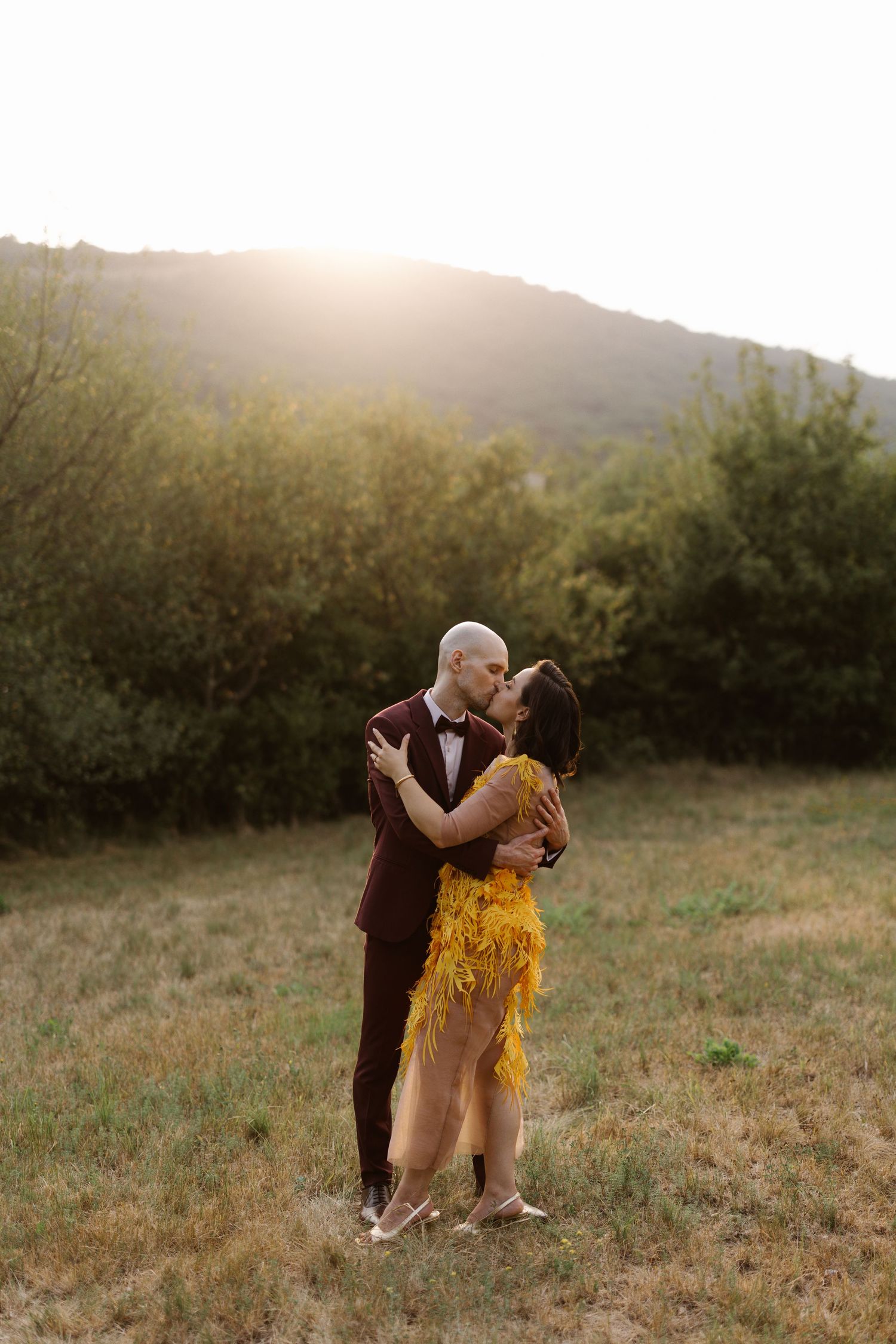 A couple in romantic embrace dances together in a sunlit meadow at golden hour.