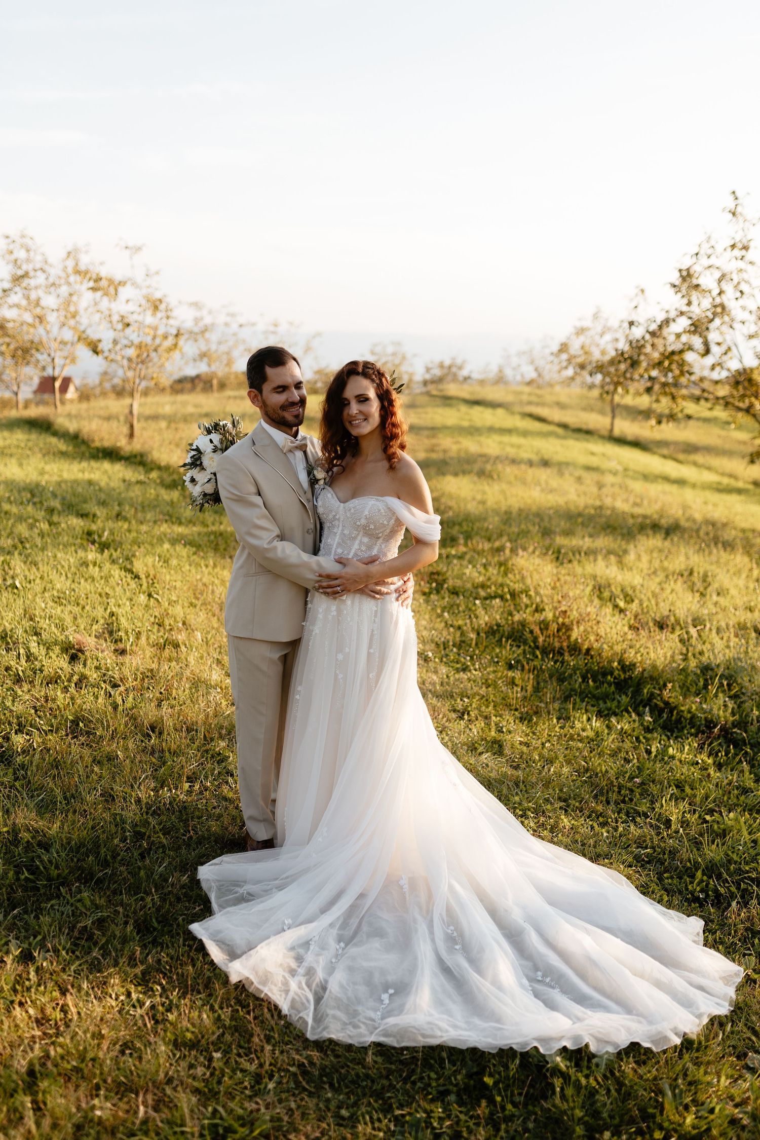 A romantic sunset wedding photoshoot in a grassy field with golden light illuminating a flowing white dress.