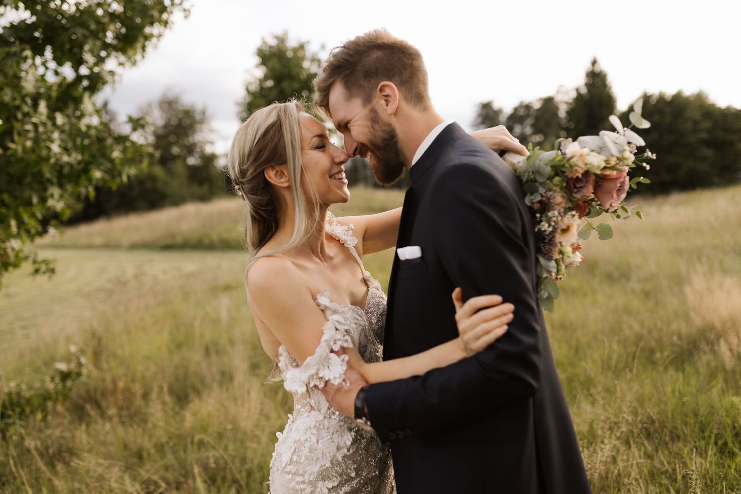 Romantic couple embracing in golden sunlit meadow during sunset photoshoot.