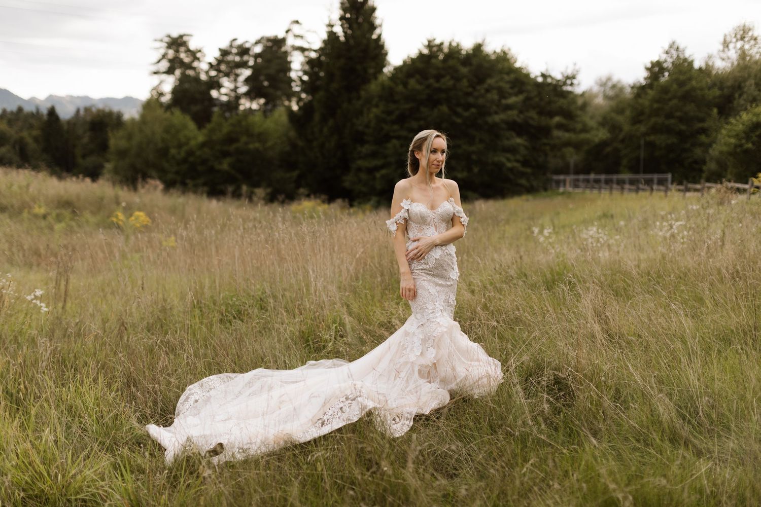 Romantic wedding couple embracing in a golden sunlit meadow with flowing white dress catching the breeze.