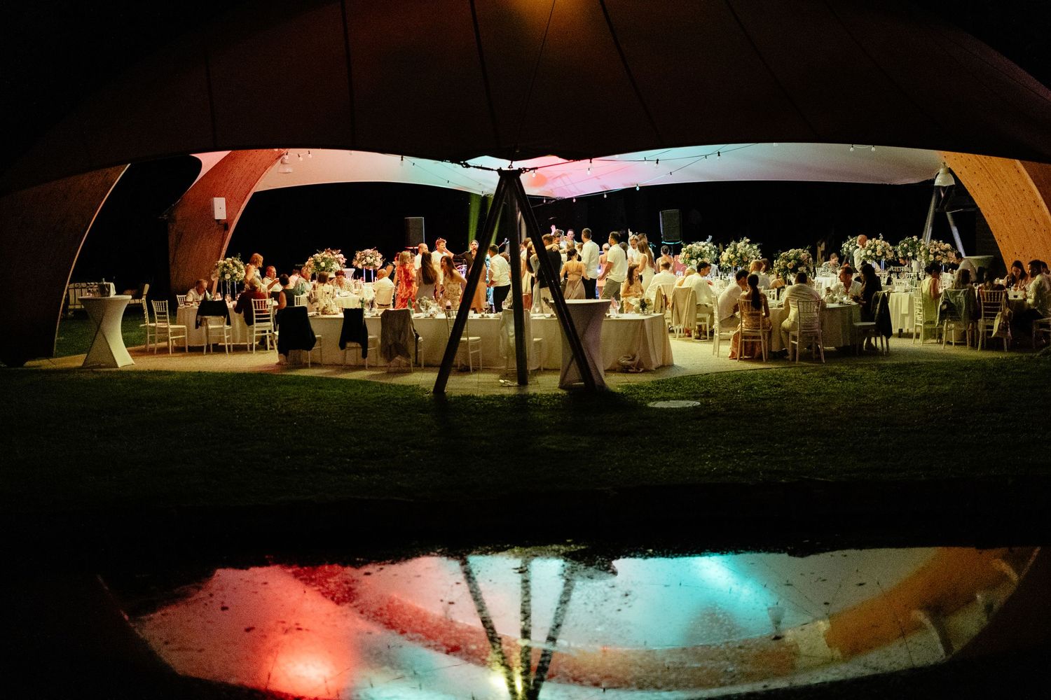 Night view of an outdoor wedding reception under illuminated tent canopies.