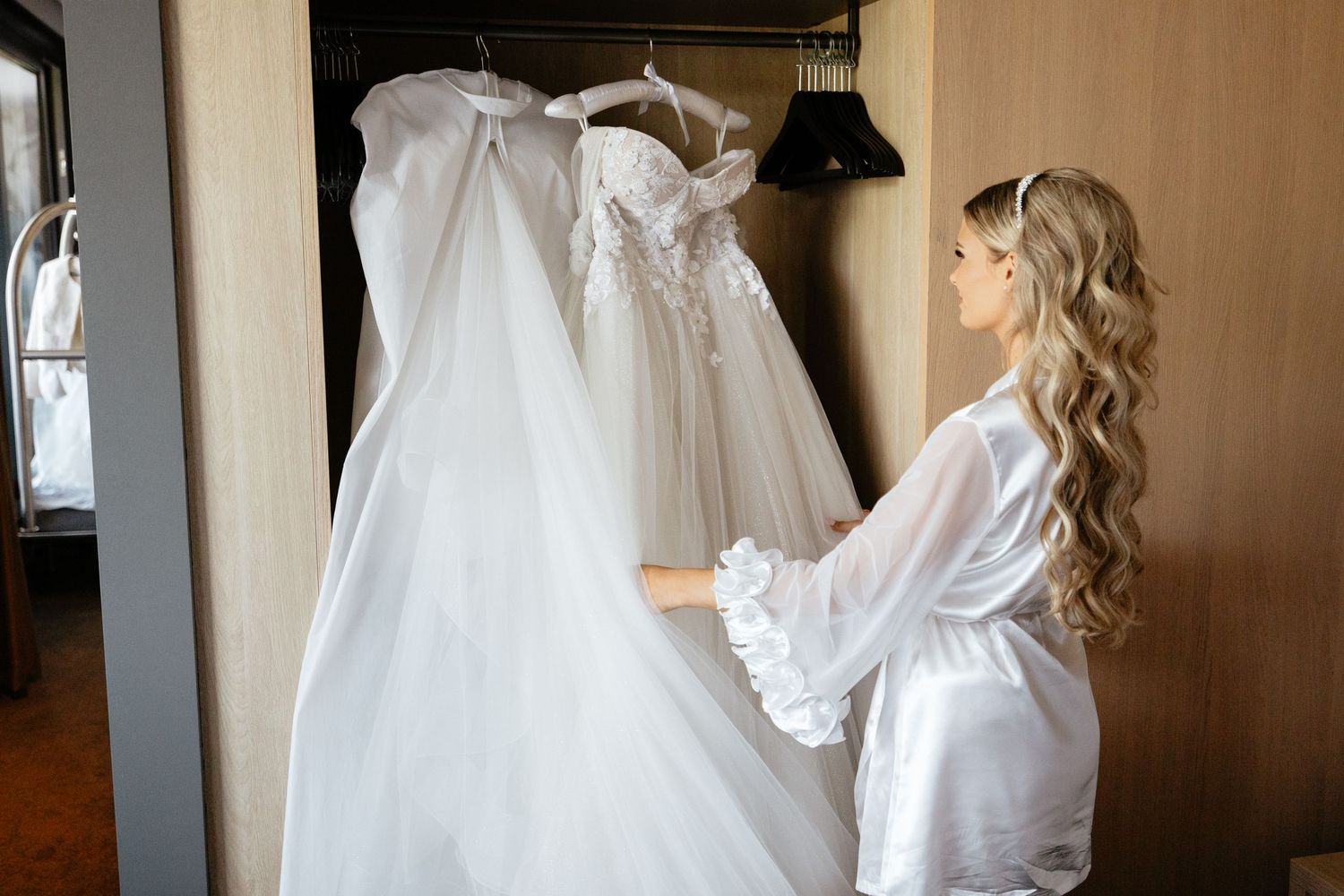 Wedding dress hangs elegantly in sunlit room during bridal preparation.