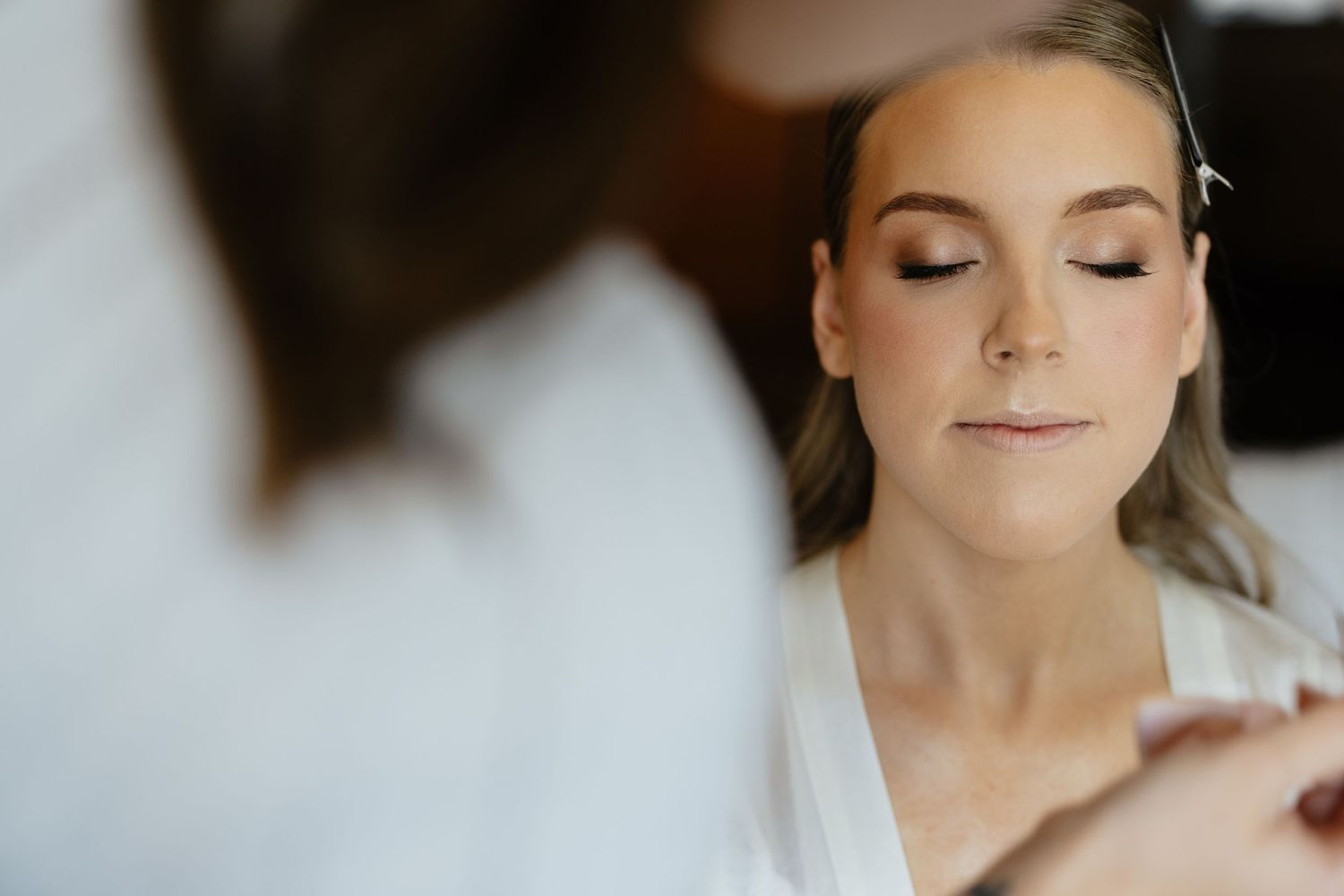 Close-up shot of bridal makeup application with eyes closed.
