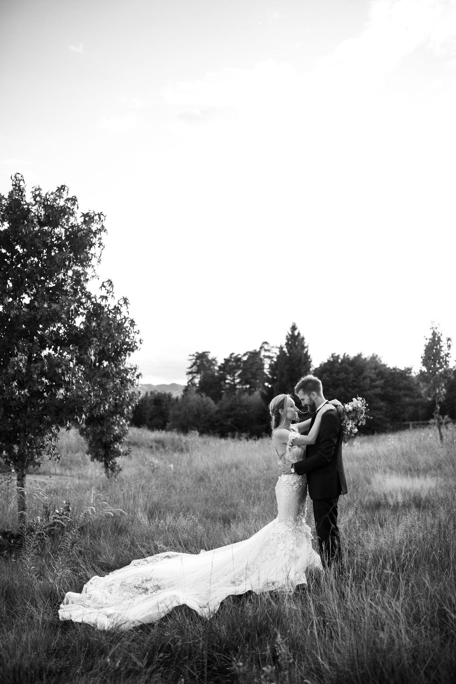 A black and white wedding portrait shows a couple dancing in a rustic field.