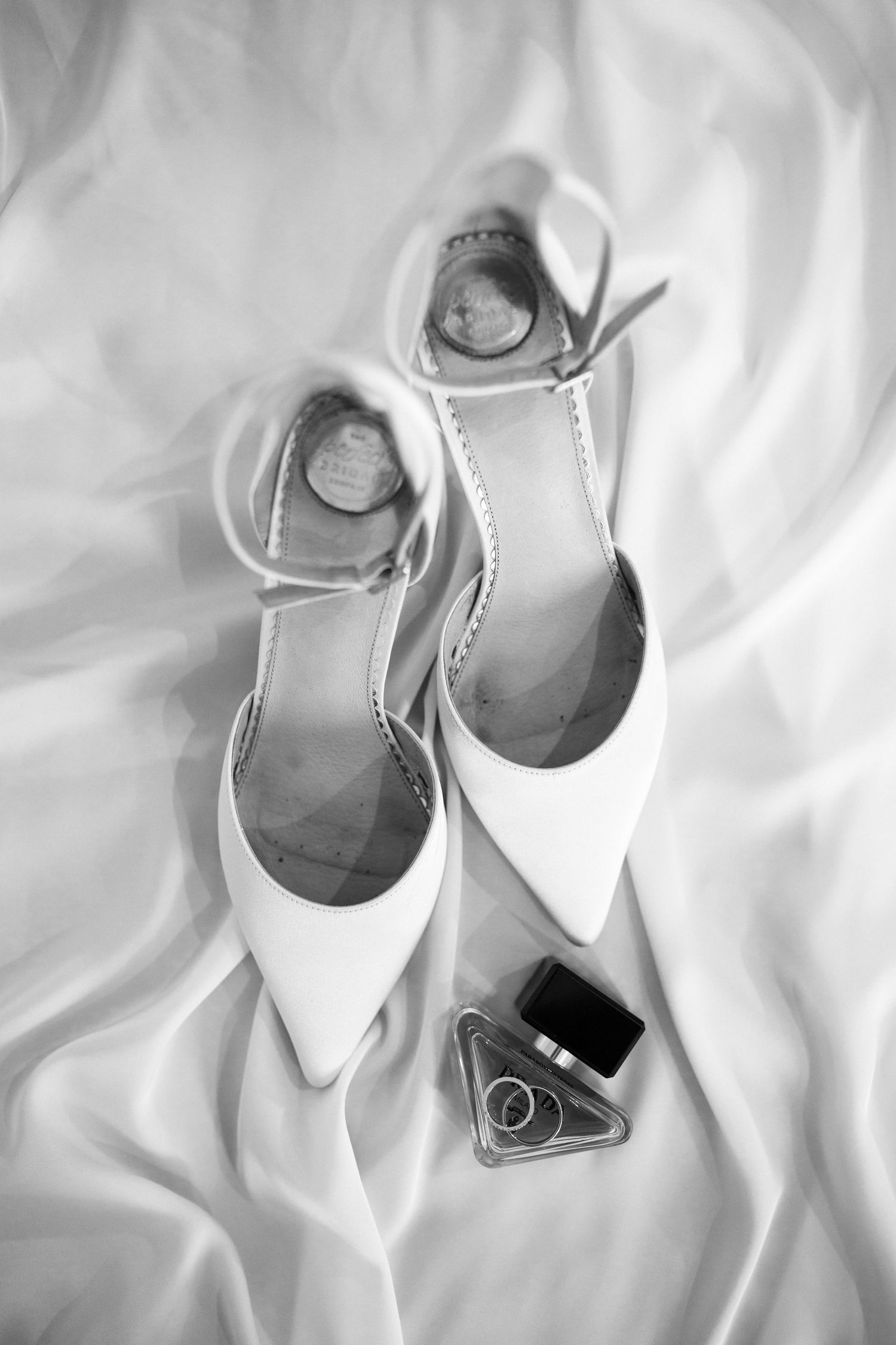 Elegant white bridal shoes arranged artistically on white fabric with soft lighting.