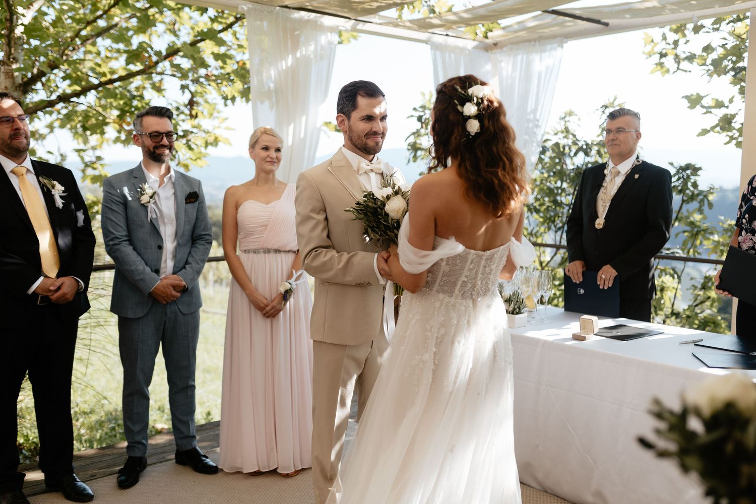 Wedding ceremony guests gather under a white tent canopy with scenic mountain views in the background.