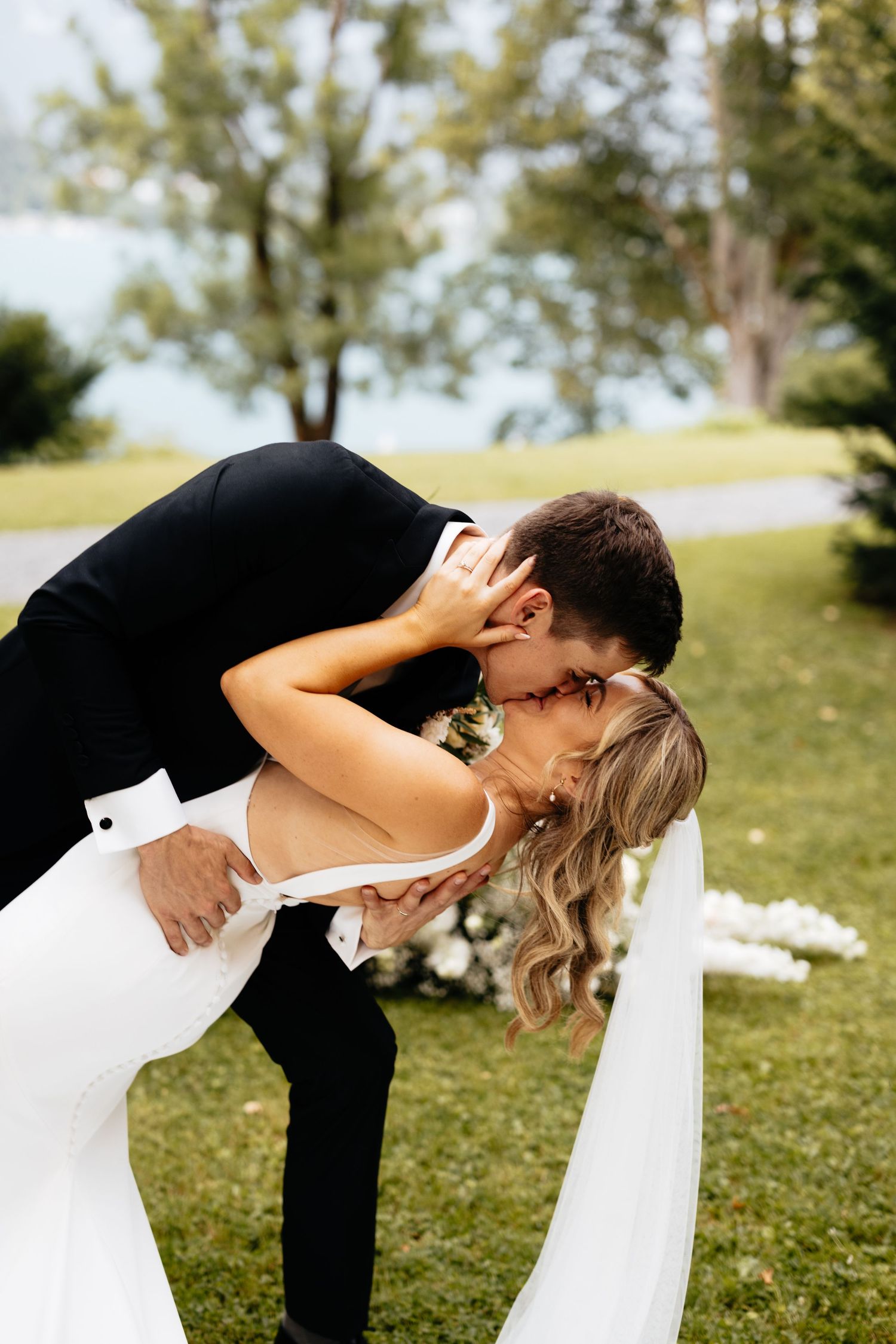 Romantic dip kiss sequence between newlyweds on a sunny lawn.