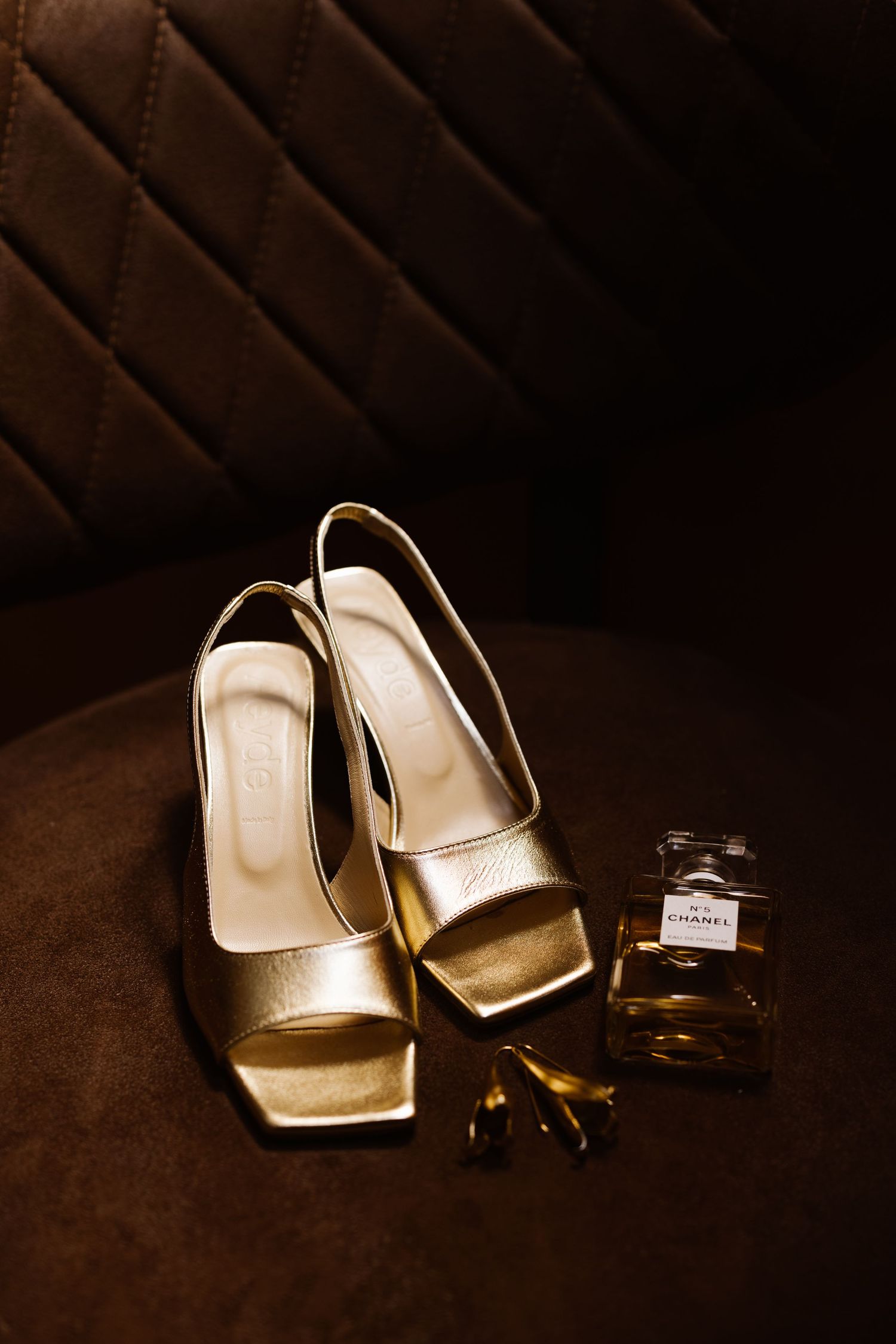 Gold bridal shoes and wedding rings arranged artistically in moody lighting.