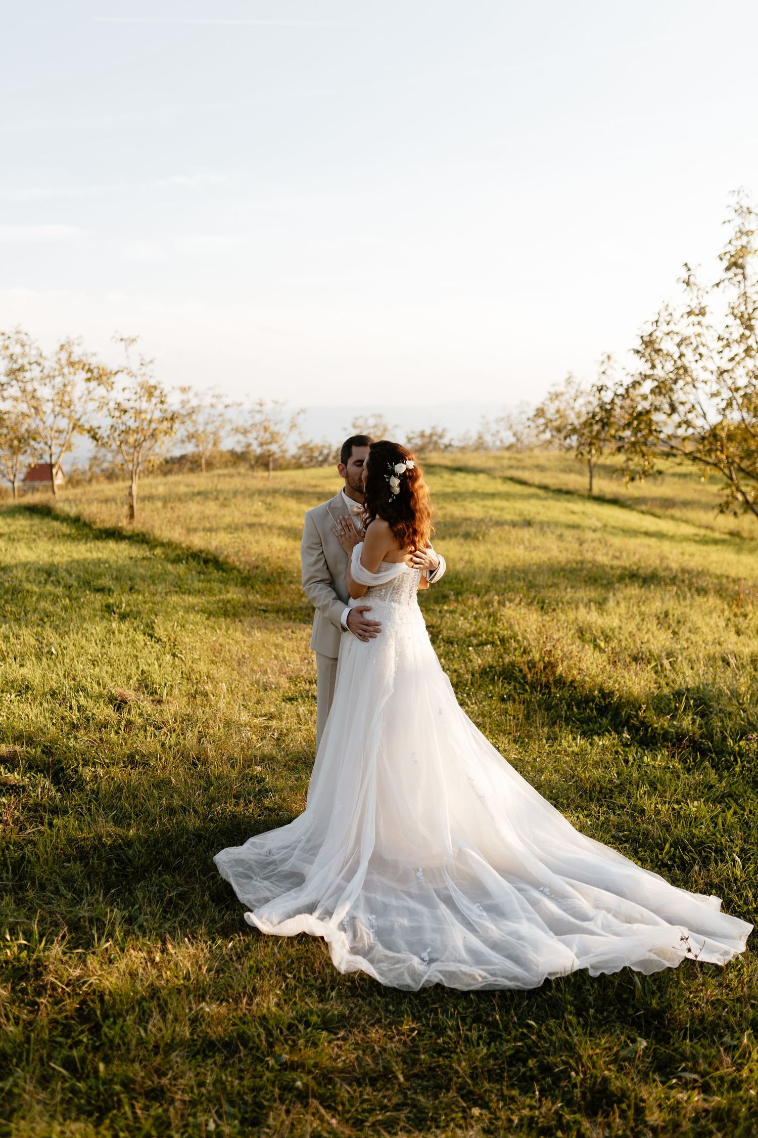 Romantic sunset wedding photos show couple embracing in golden light on grassy hillside with flowing white dress.