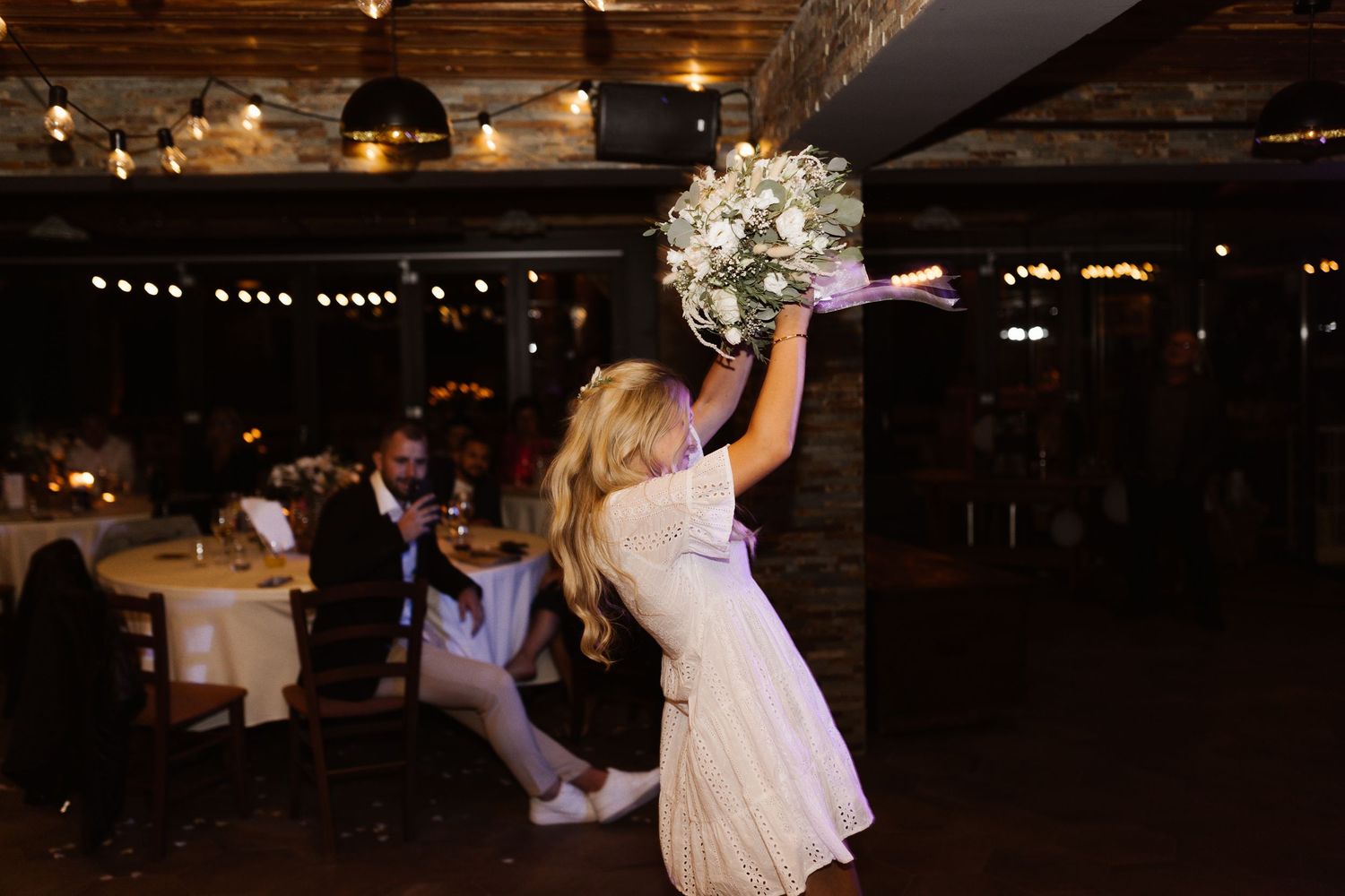 A festive wedding reception dance floor illuminated by overhead string lights and decorative floral arrangements.