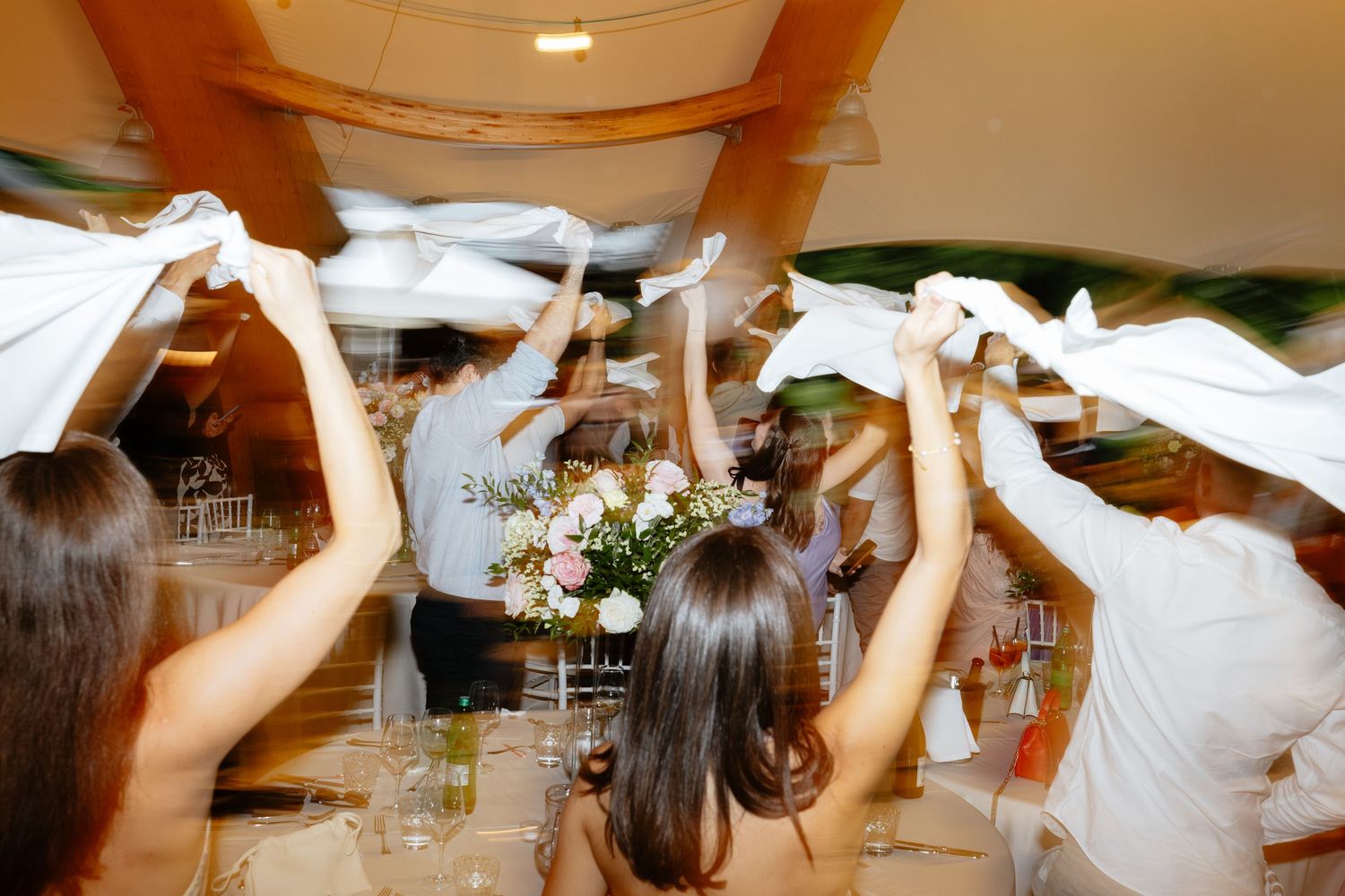 Wedding guests dancing with raised arms on a reception dance floor under warm lighting.