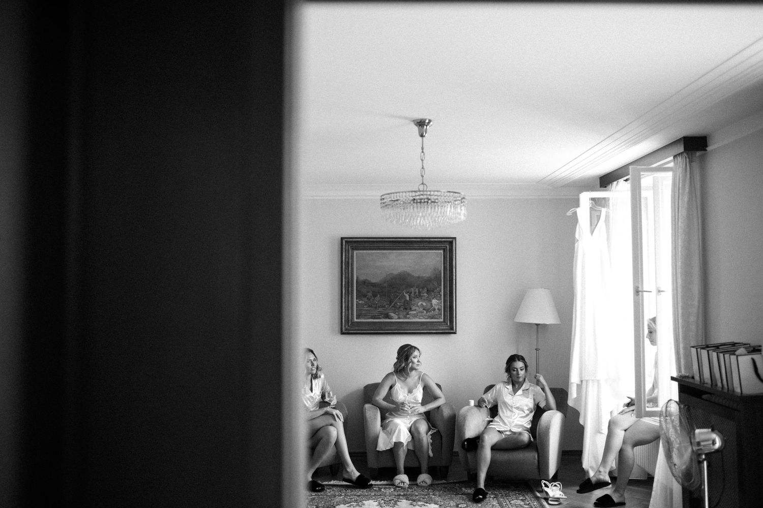 Black and white image showing people seated in a bright interior room with windows and artwork.