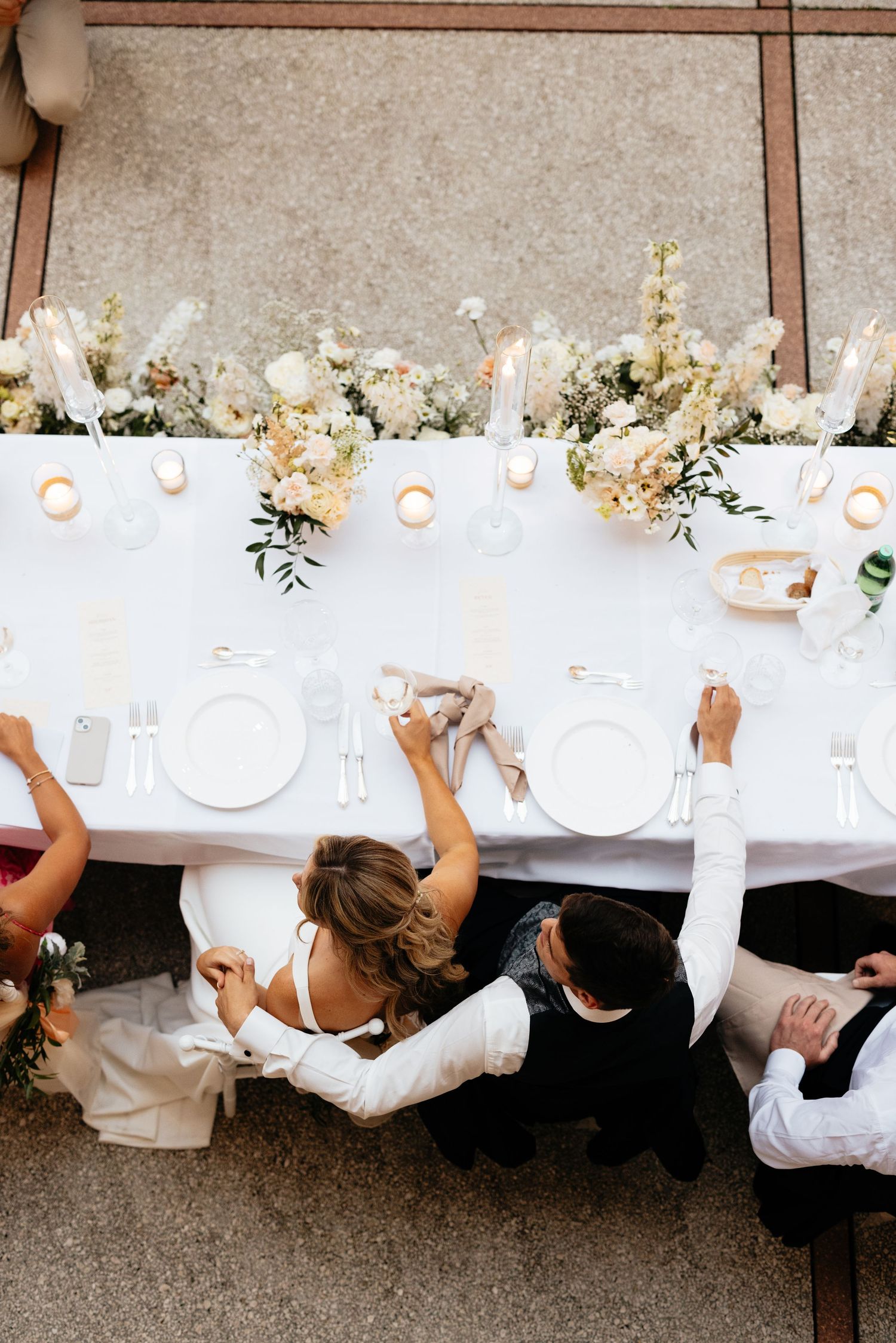 Wedding party members seated at a long white-clothed dining table captured from an overhead view.