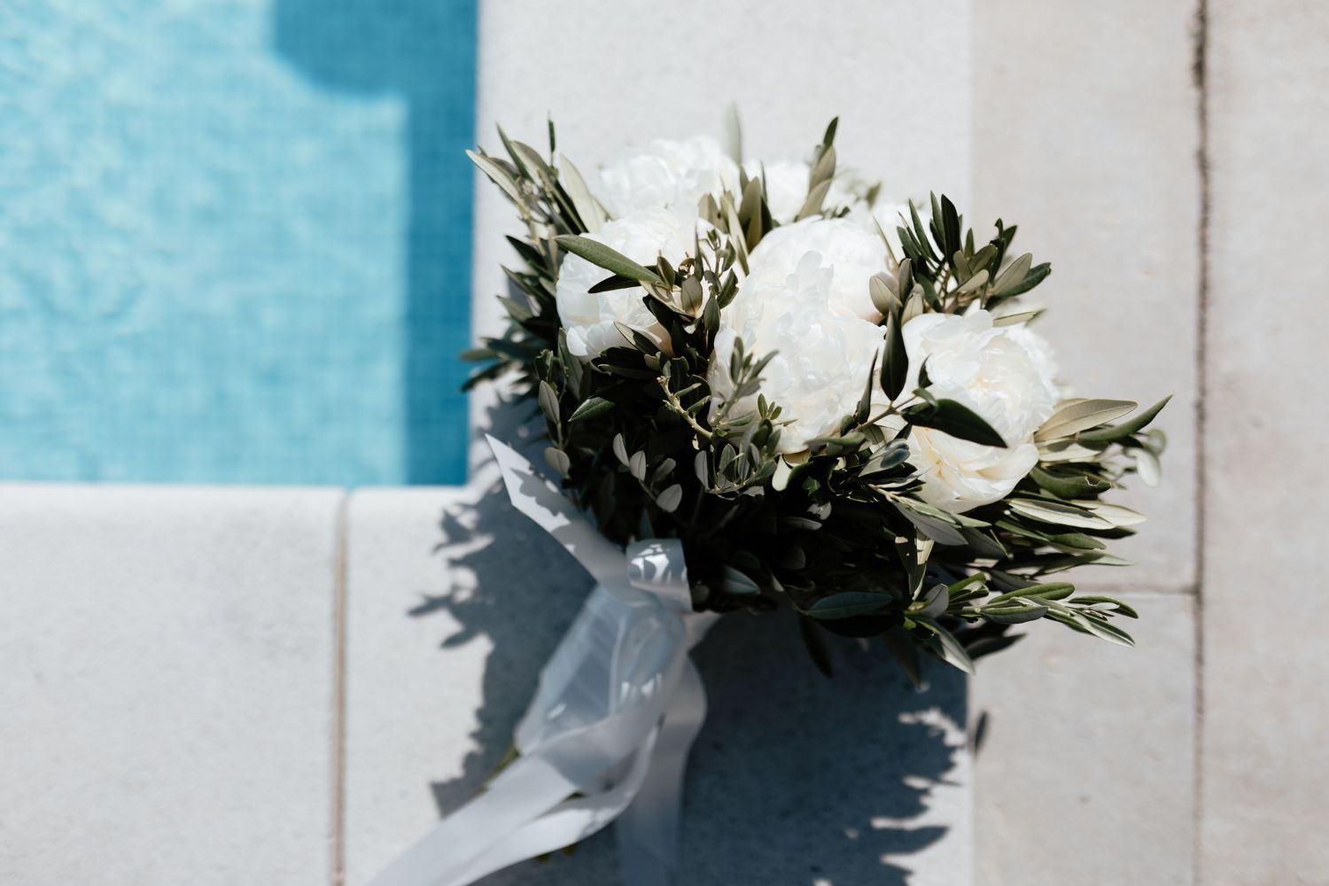 White floral bouquet with greenery rests against a light blue wall creating an elegant wedding detail.