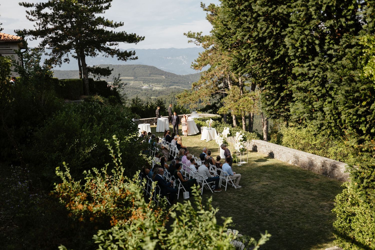 Outdoor wedding ceremony setup with white chairs and natural greenery backdrop.
