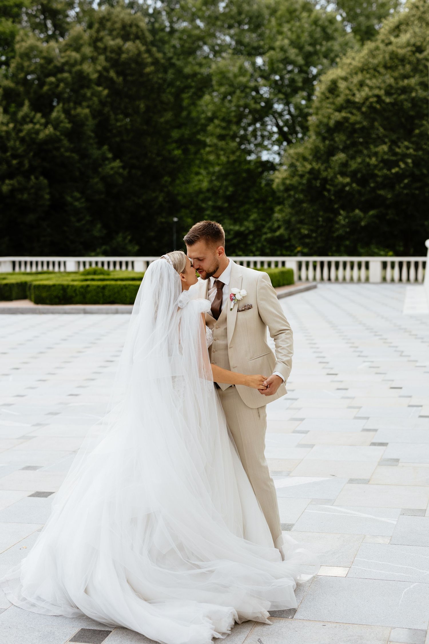 A romantic wedding couple shares intimate moments on a white stone patio surrounded by lush greenery.