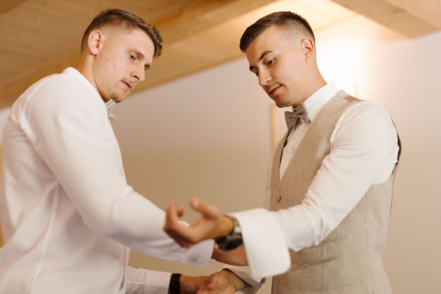 Two people in formal white attire adjusting their sleeves and cuffs while getting ready for a special occasion.
