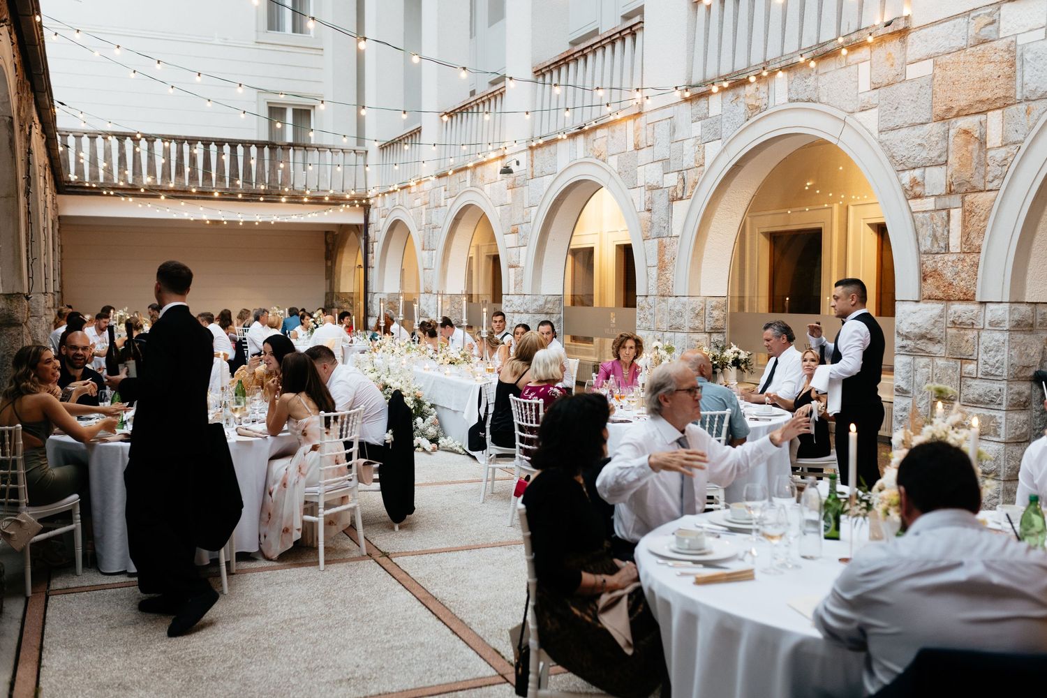 Elegant wedding reception setup with round tables and stone archways in a rustic venue.