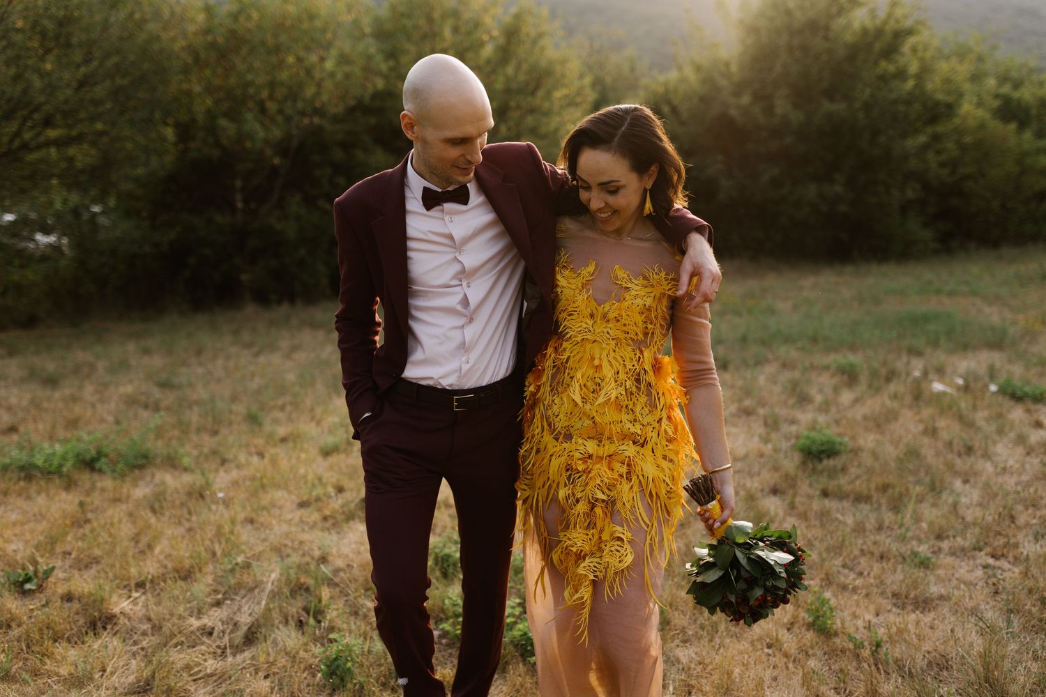 Couple walking together through a scenic outdoor field at sunset with mountains in the background.