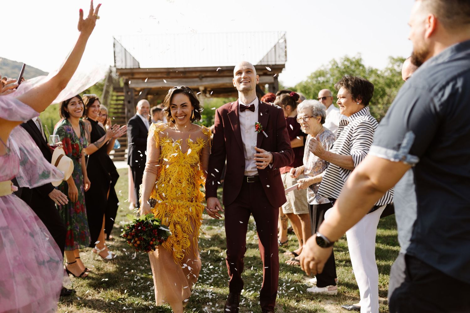 Wedding guests celebrate with a couple during an outdoor ceremony in warm sunlight.