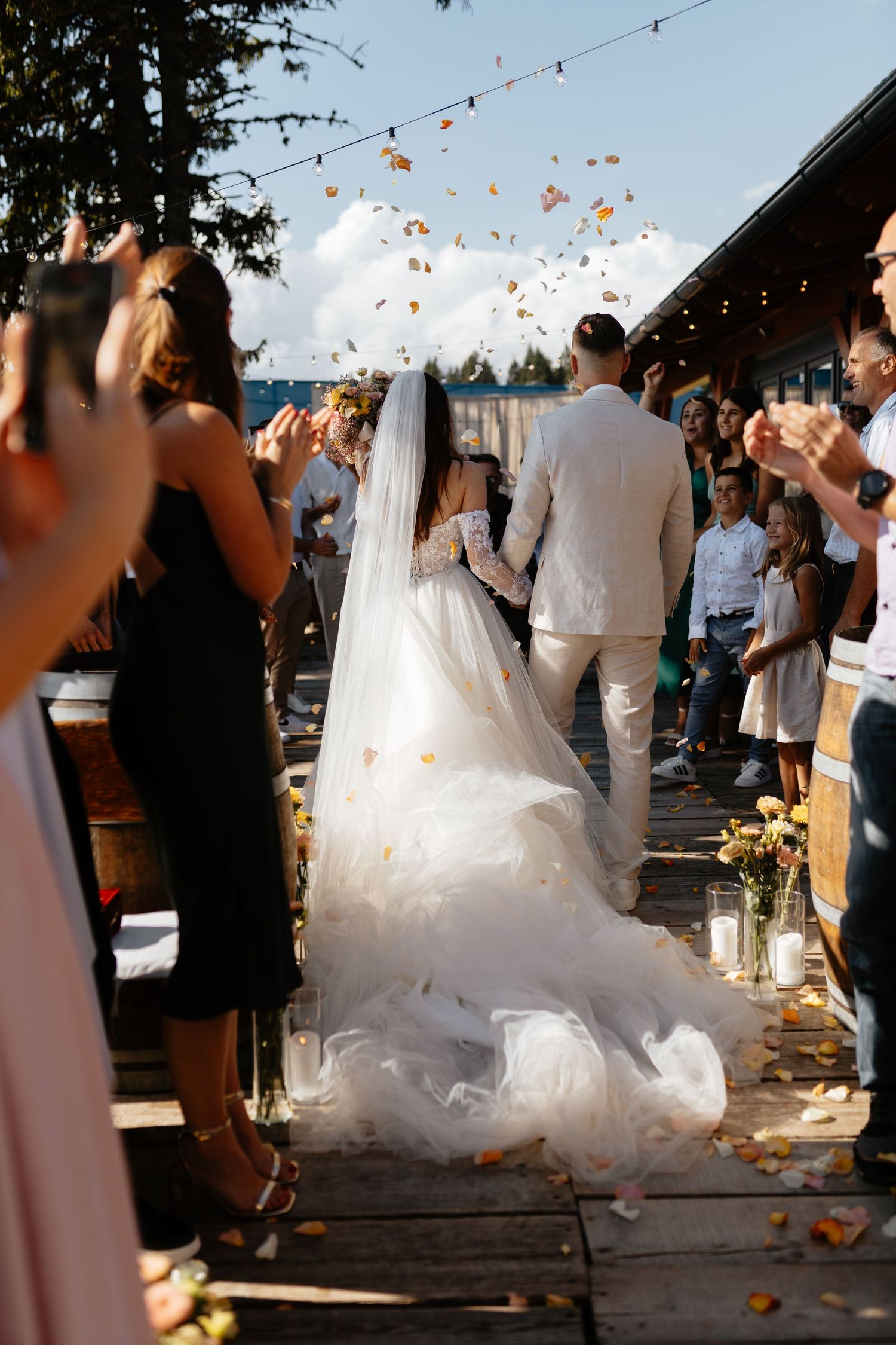 Wedding celebration outdoors with string lights as guests throw flower petals.
