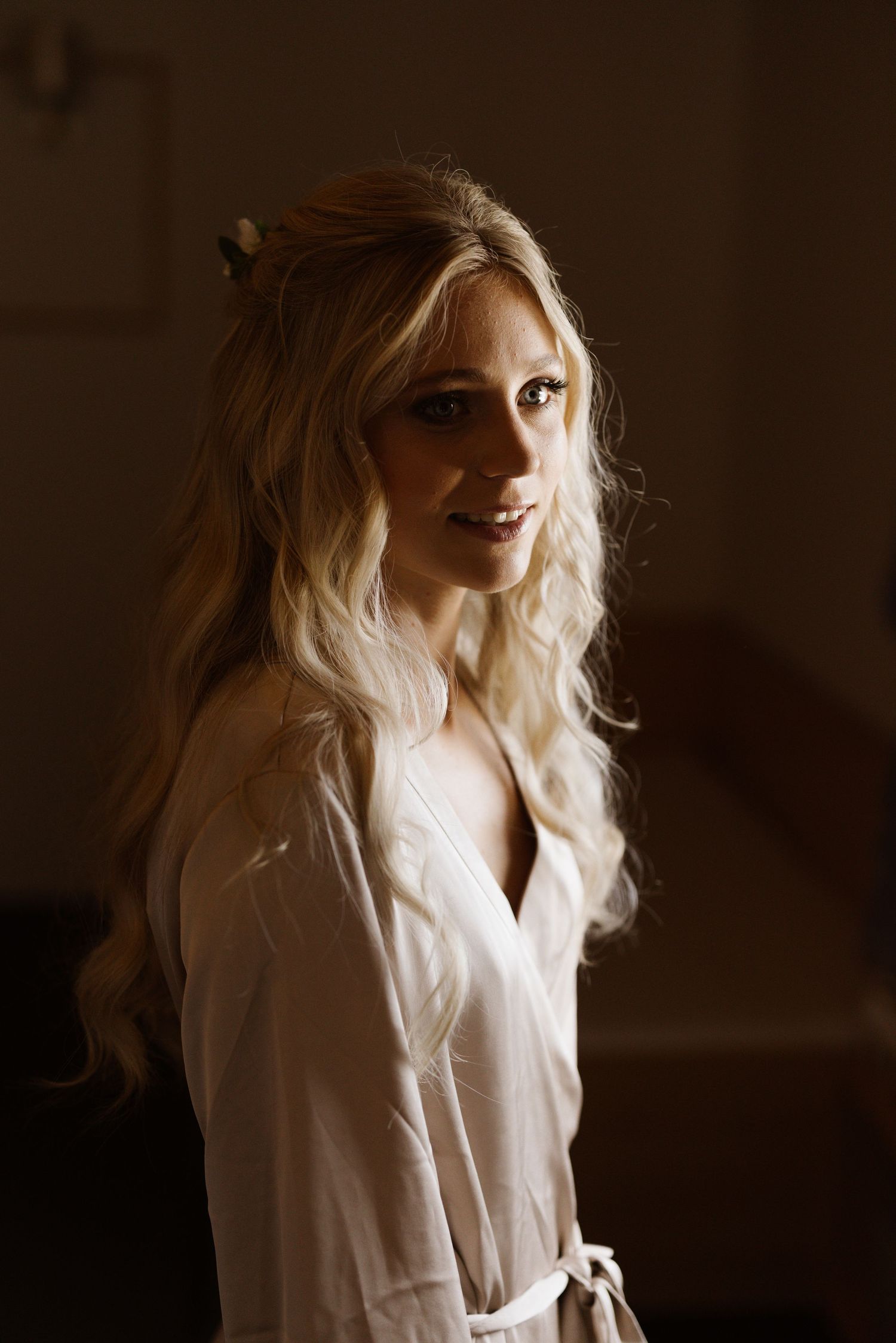 A moody portrait of a woman in white wearing a robe with soft lighting and dark background.