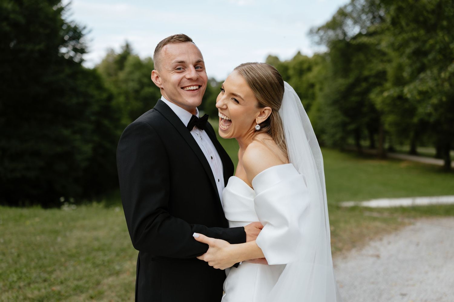 Joyful wedding couple sharing intimate moments on a path surrounded by greenery.