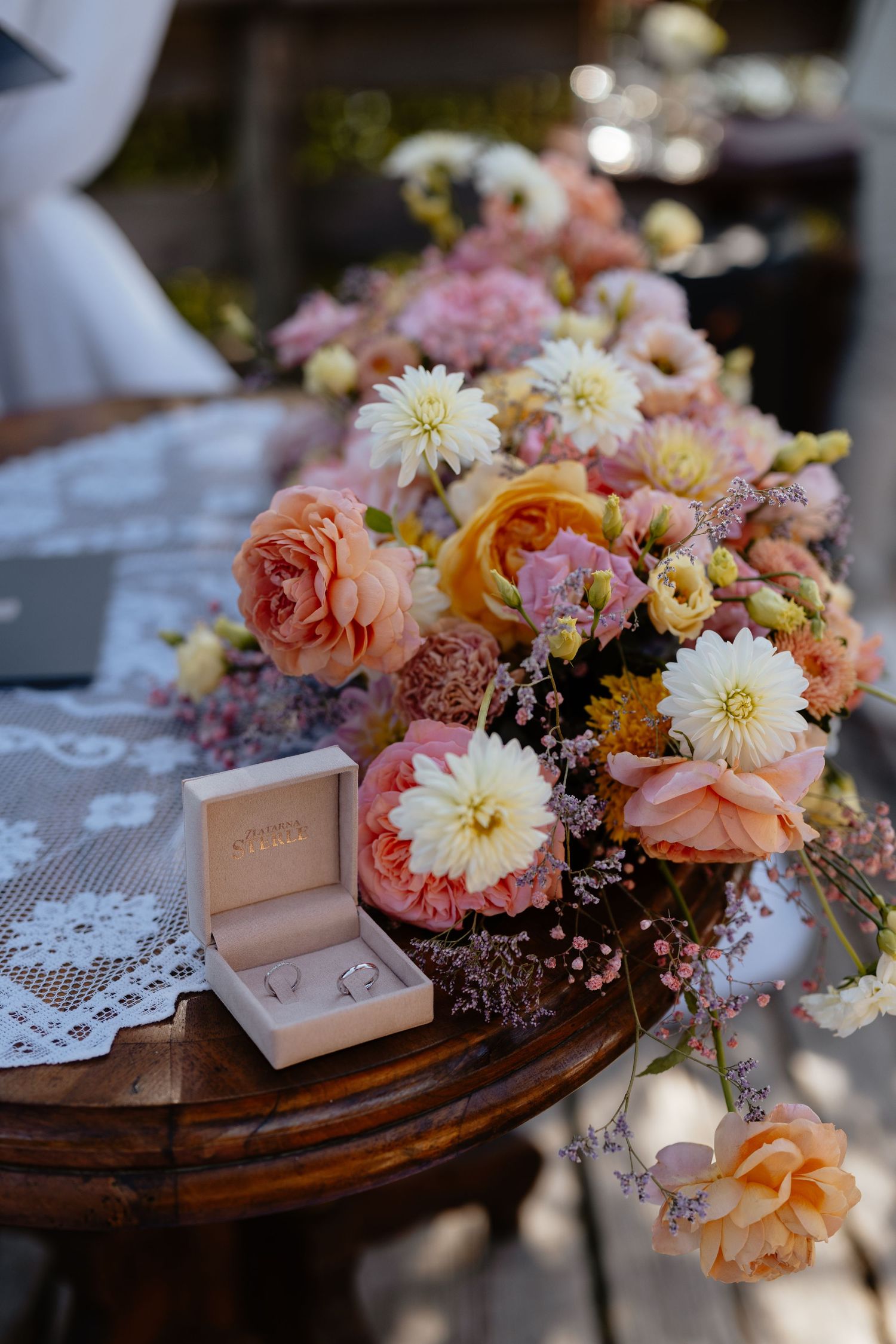Romantic floral arrangement with peach and white blooms alongside a ring box on a wooden surface.