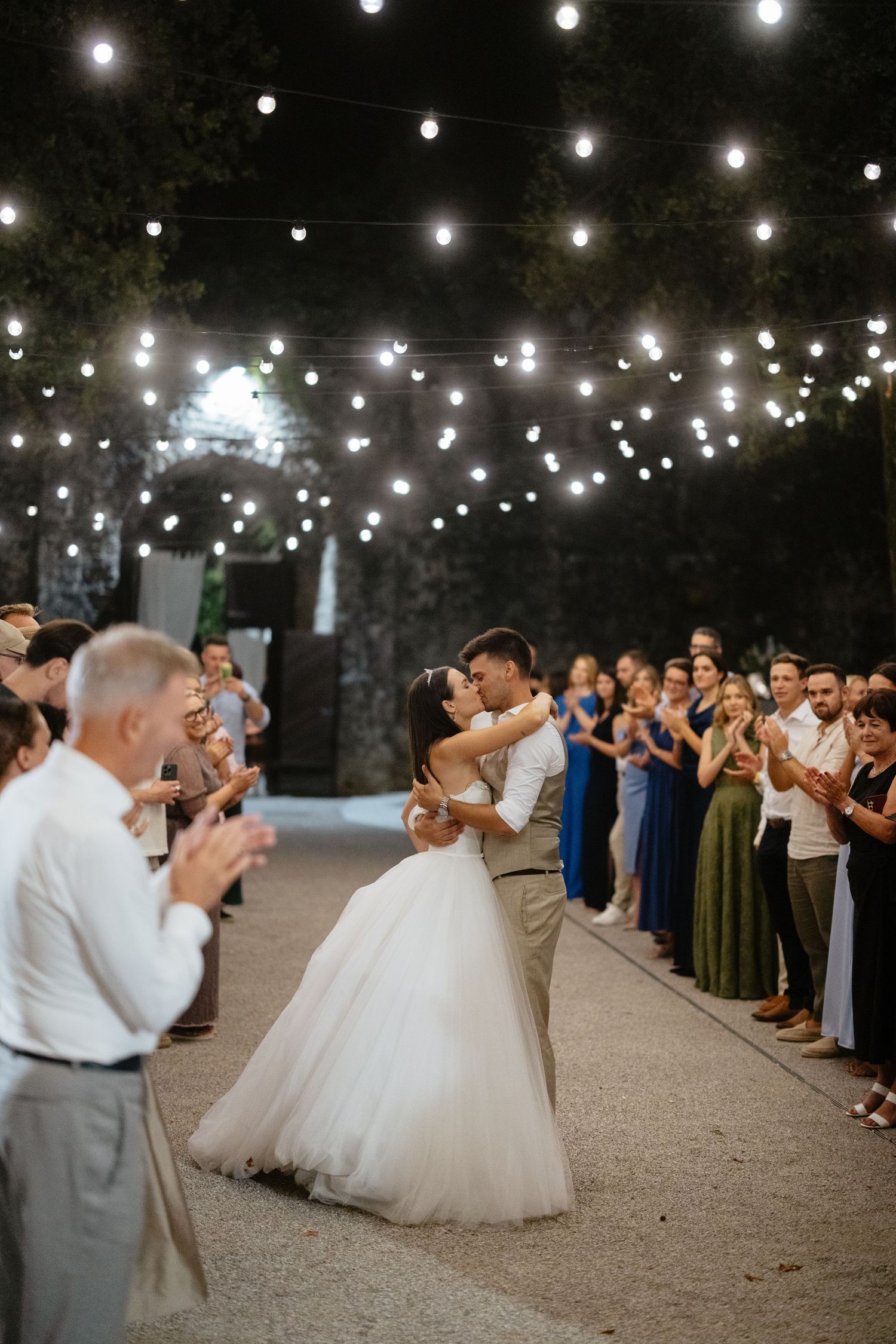 Wedding guests form lines for a dance under string lights at an outdoor reception.