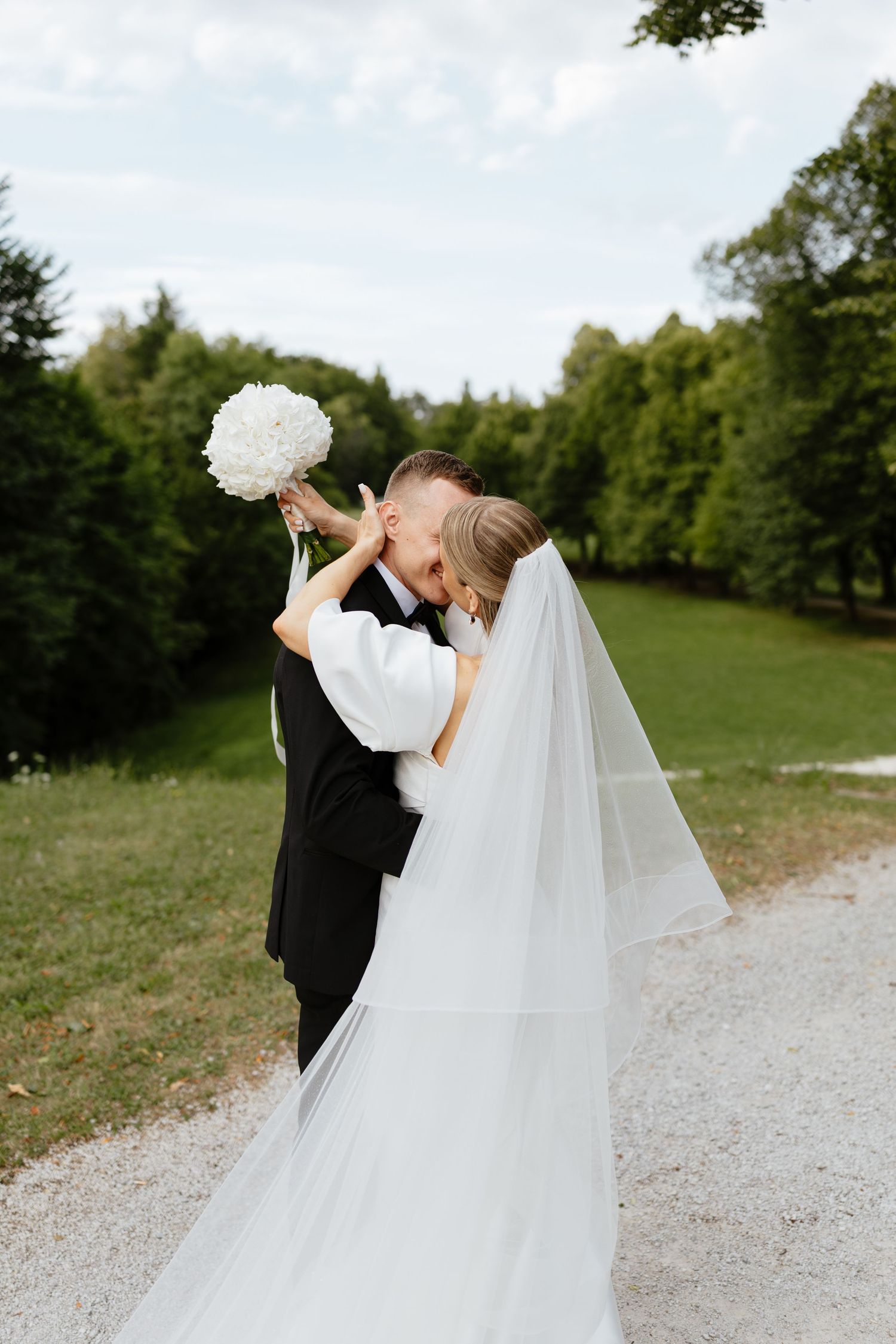 Romantic wedding couple dancing and twirling on a gravel path surrounded by green trees.