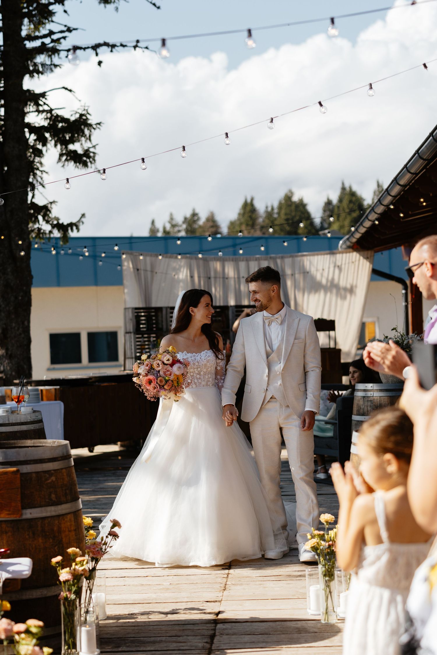 Newlyweds share intimate moments during their outdoor wedding reception under string lights at dusk.