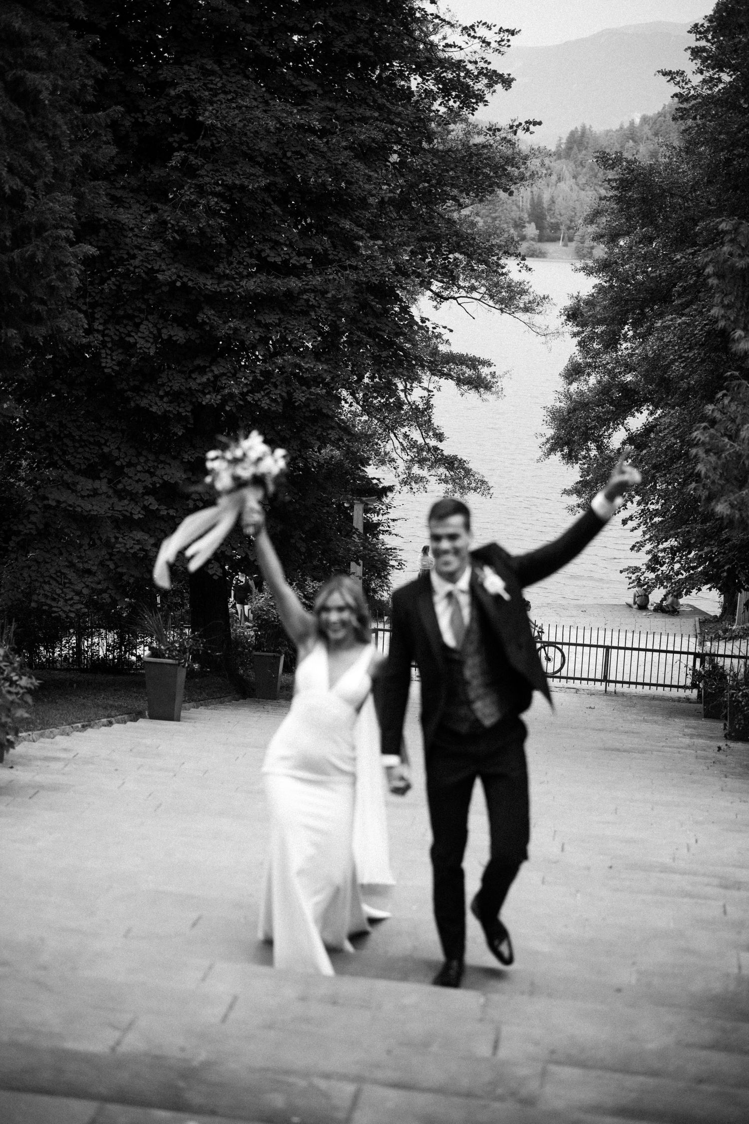 A joyful celebration moment captured in black and white as newlyweds celebrate walking down a scenic path.