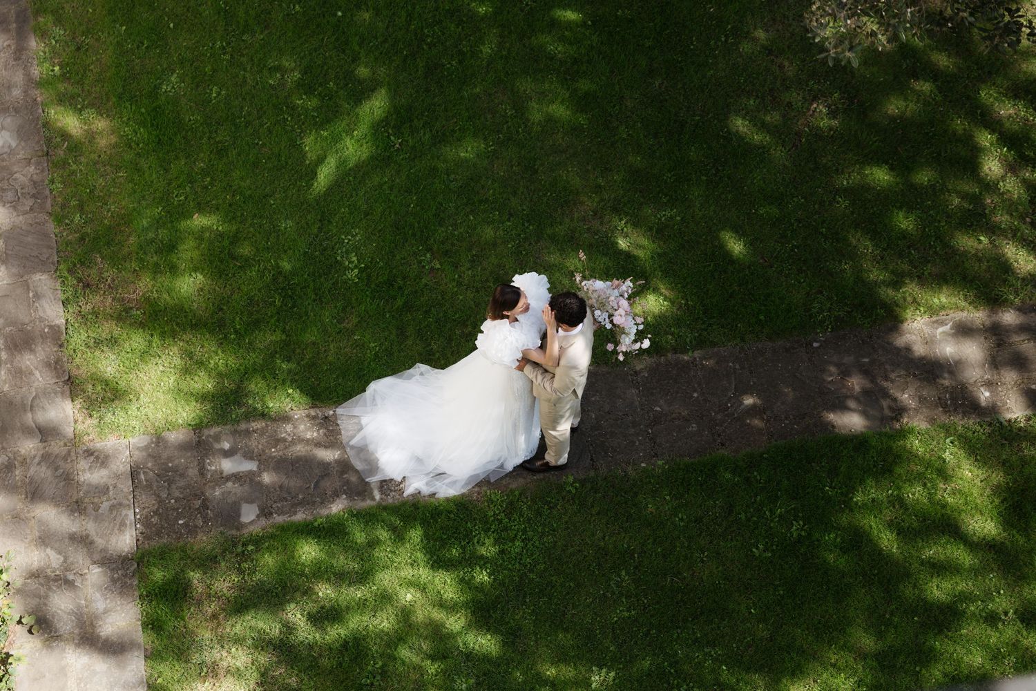 A couple in wedding attire walks through a lush garden path surrounded by greenery and natural scenery.