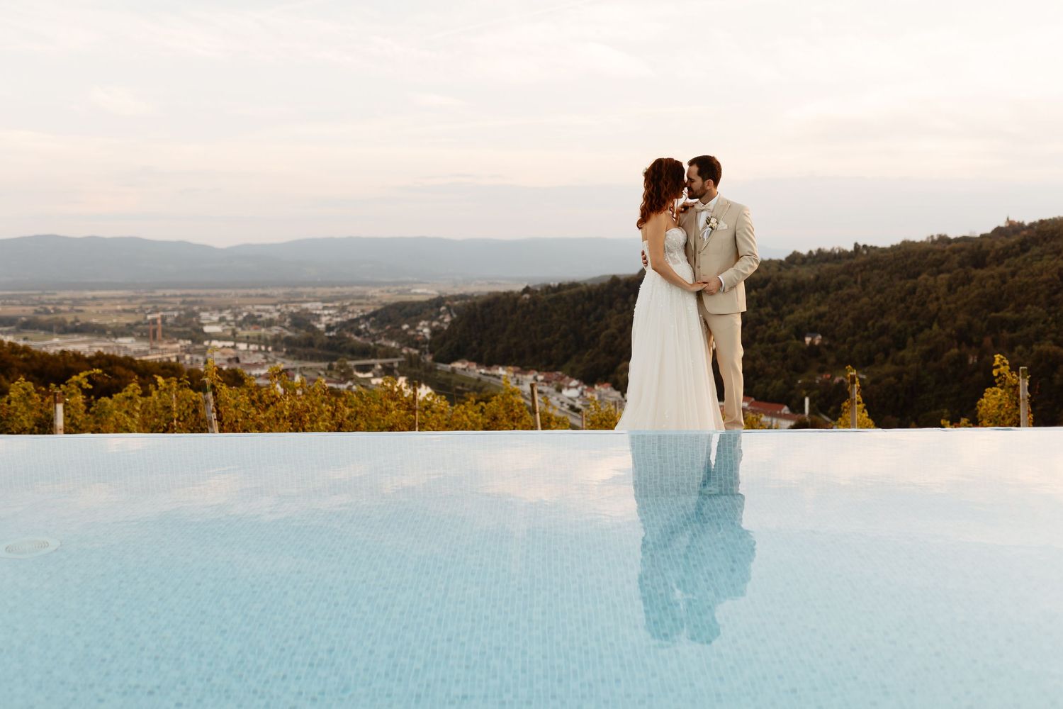 A scenic wedding portrait overlooking mountains and water with a sunset glow creating a dreamy atmosphere.