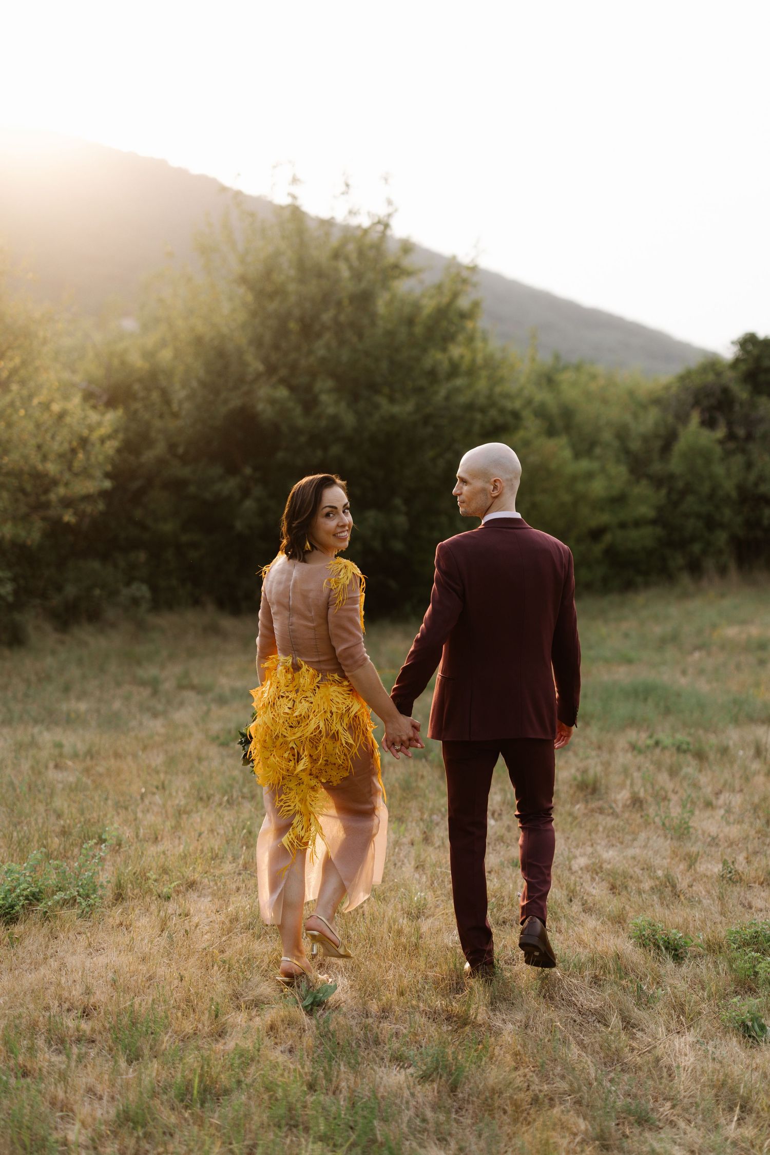 Couple walking through a golden field at sunset wearing formal attire.