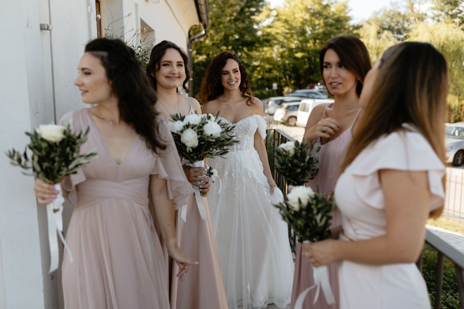 Bridesmaids in blush pink dresses gather together outdoors for a wedding photo.