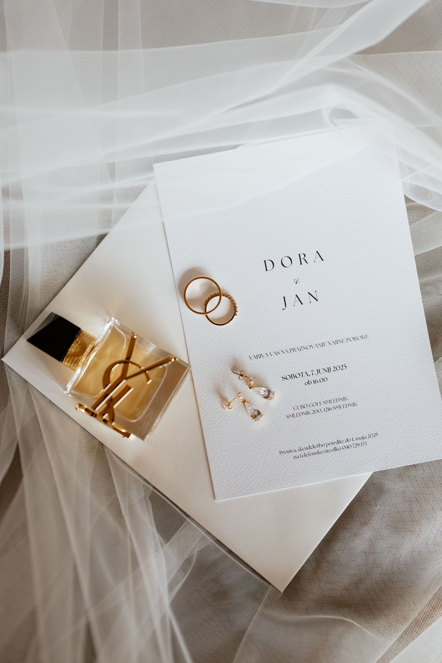 Elegant wedding invitation cards with gold lettering and wedding rings displayed on white fabric.