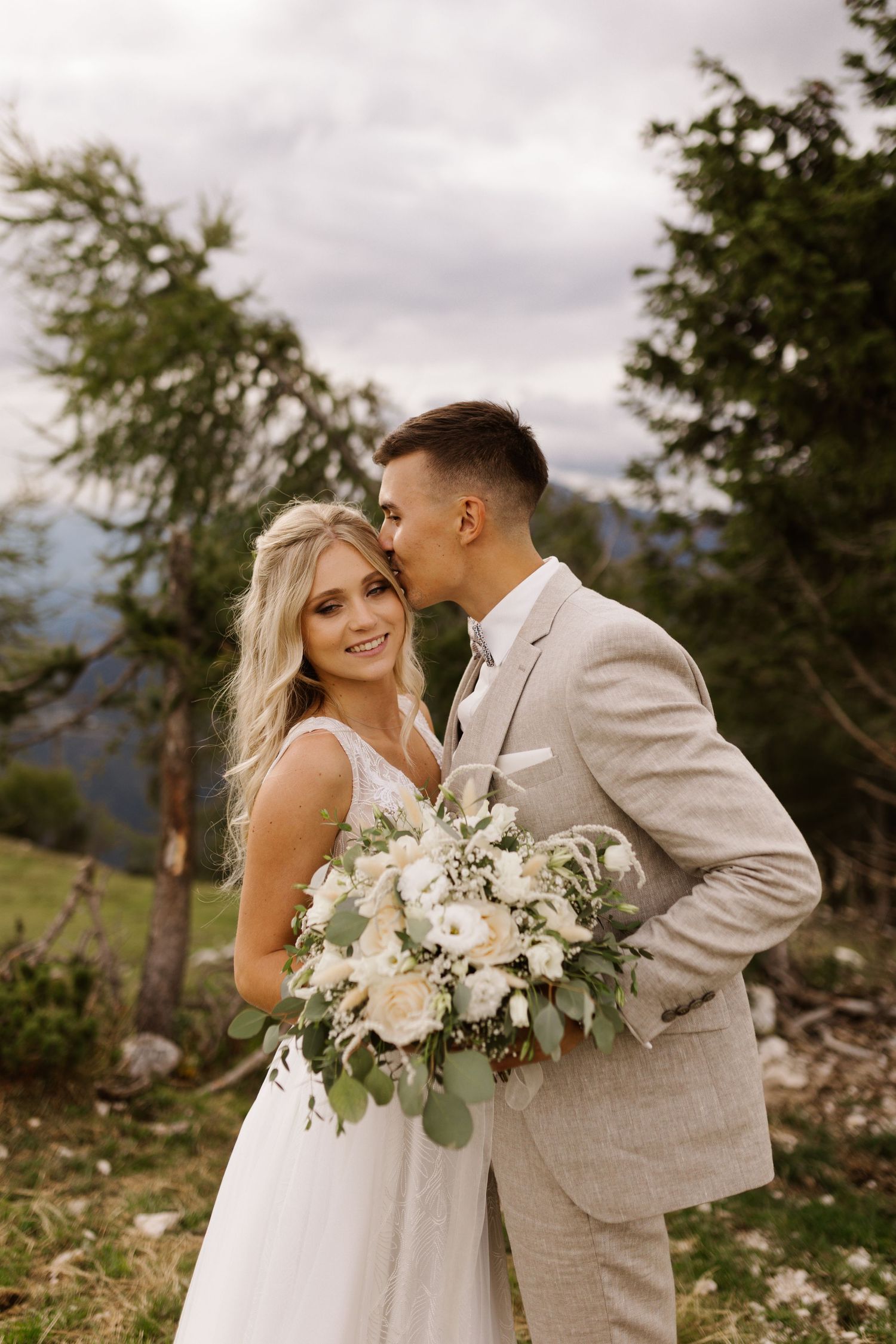 A couple shares romantic moments during their mountain wedding photoshoot with white floral bouquet.