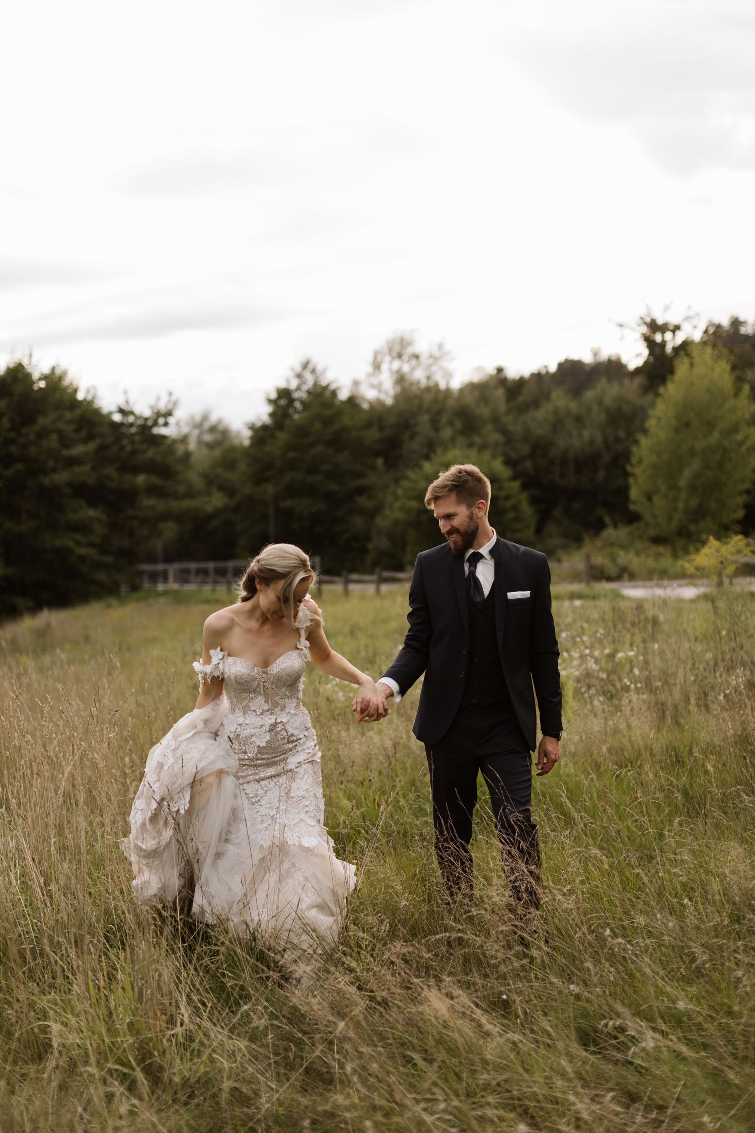 A couple walking through a rustic field with tall grass during their wedding photoshoot.