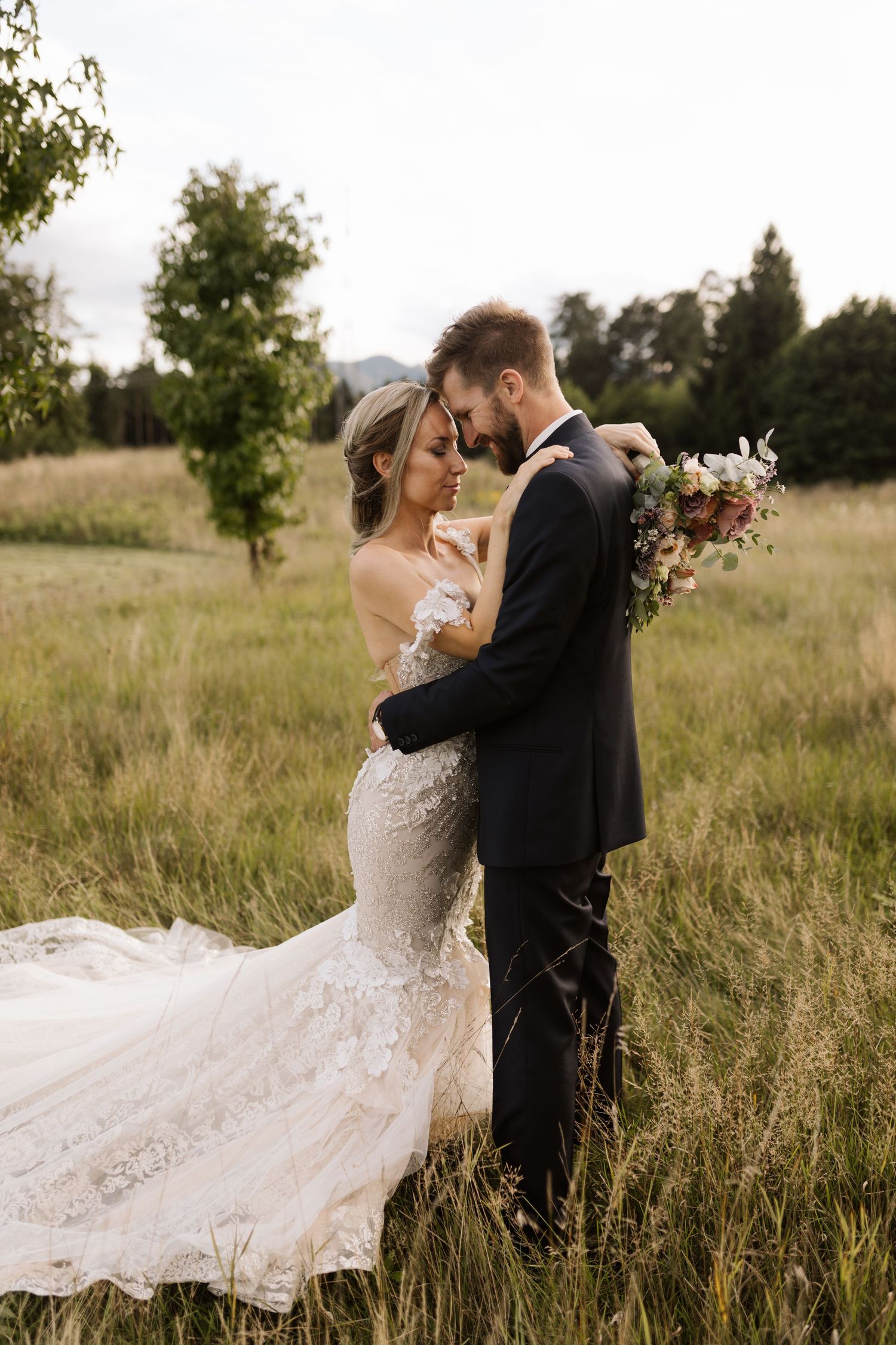 A newlywed couple shares an intimate moment in a golden field during sunset while the bride's dress flows in the wind.