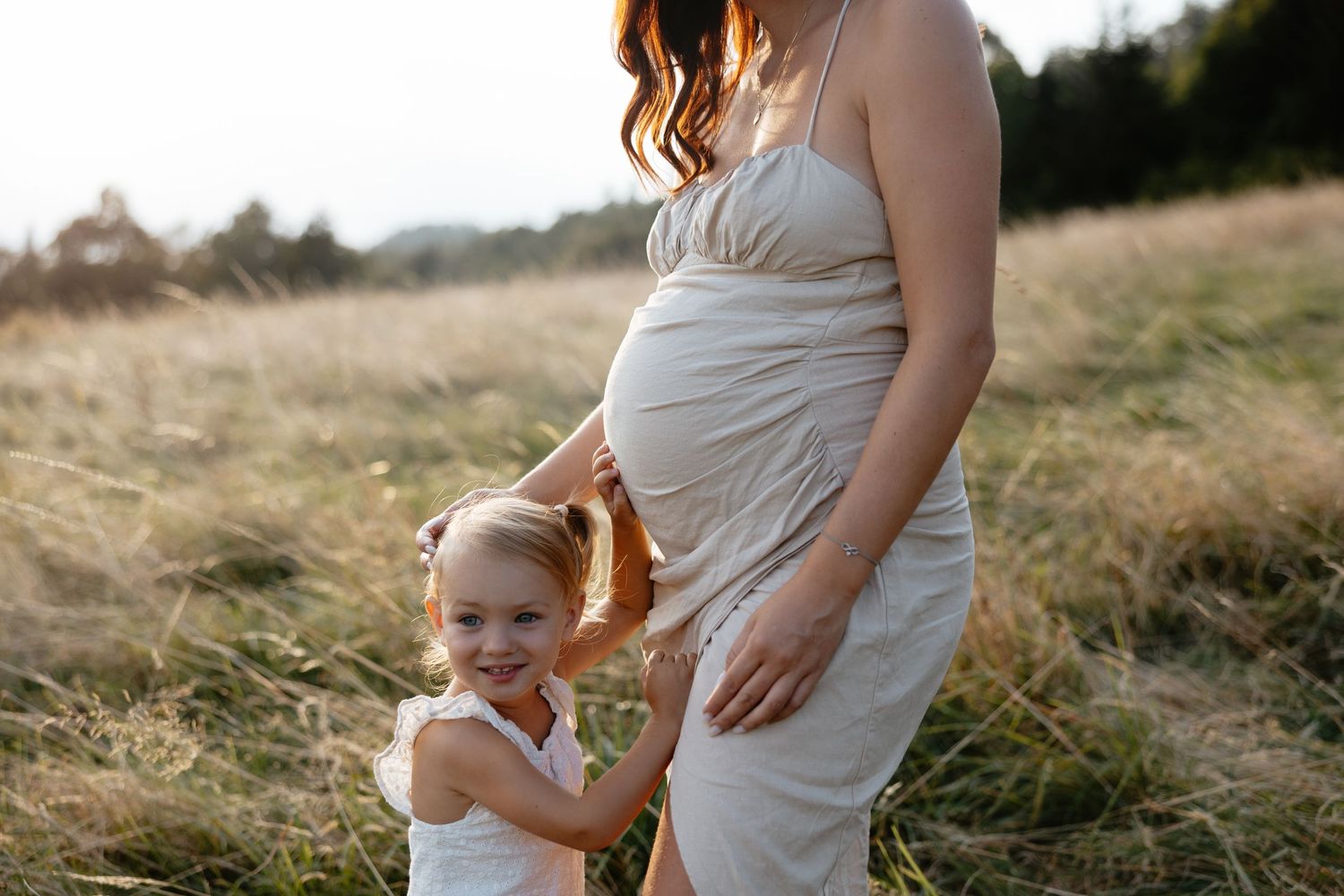 A tender moment between parent and child wearing matching white dresses in a grassy meadow.